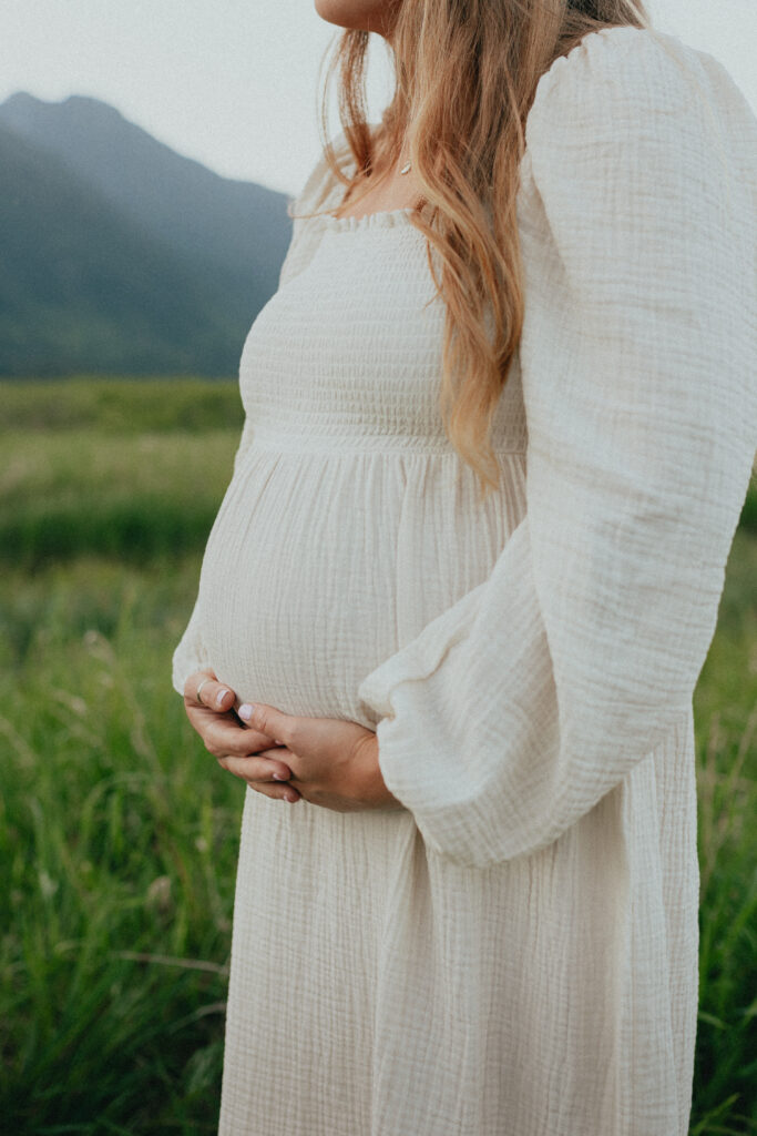 photo of a mom cradling her baby bump in a white dress taken outside in a field in langley