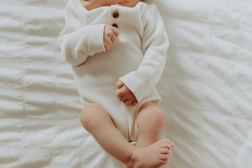 photo a newborn baby focused on their little hands and feet while they are laying on a bed with white sheets taken in langley