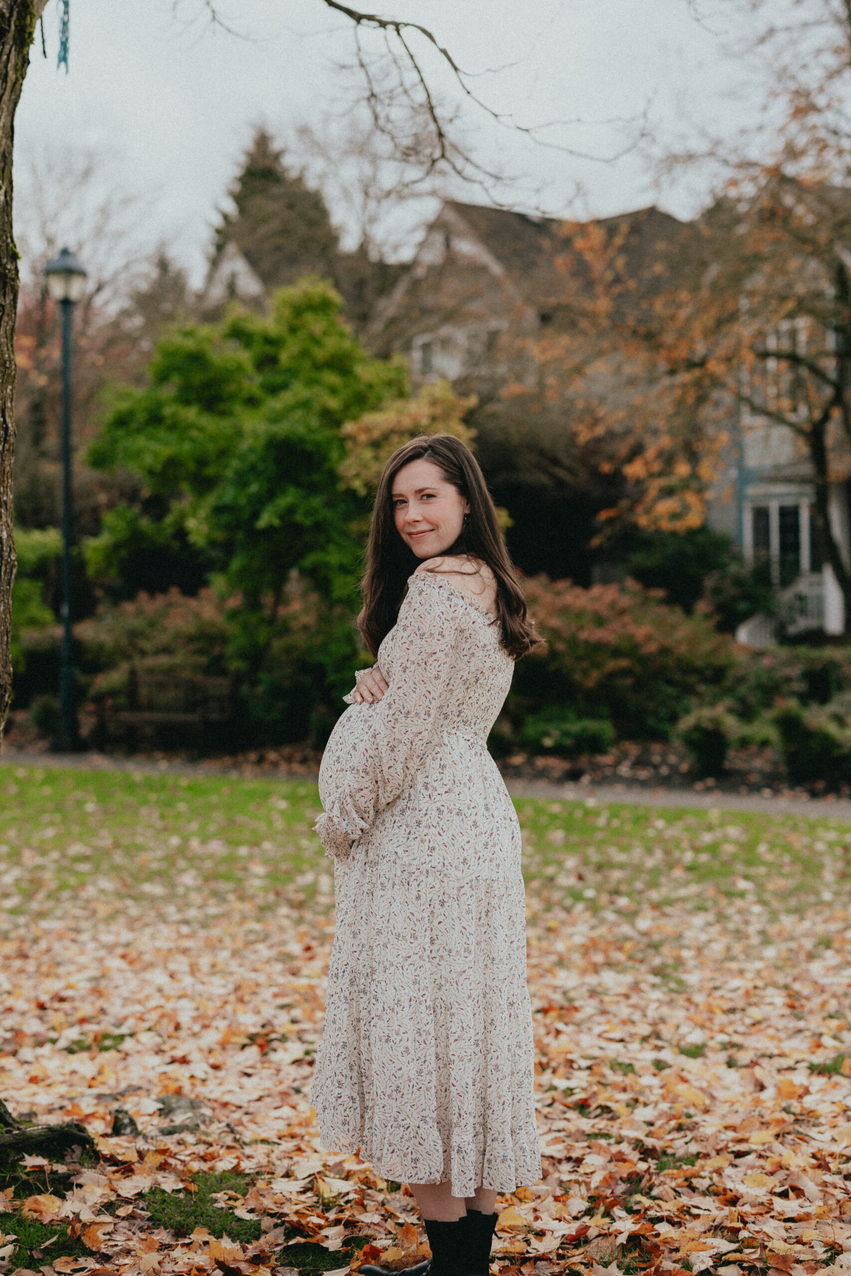 photo of a pregnant woman surrounded by fall leaves taken from the side while she looks down with her eyes closed