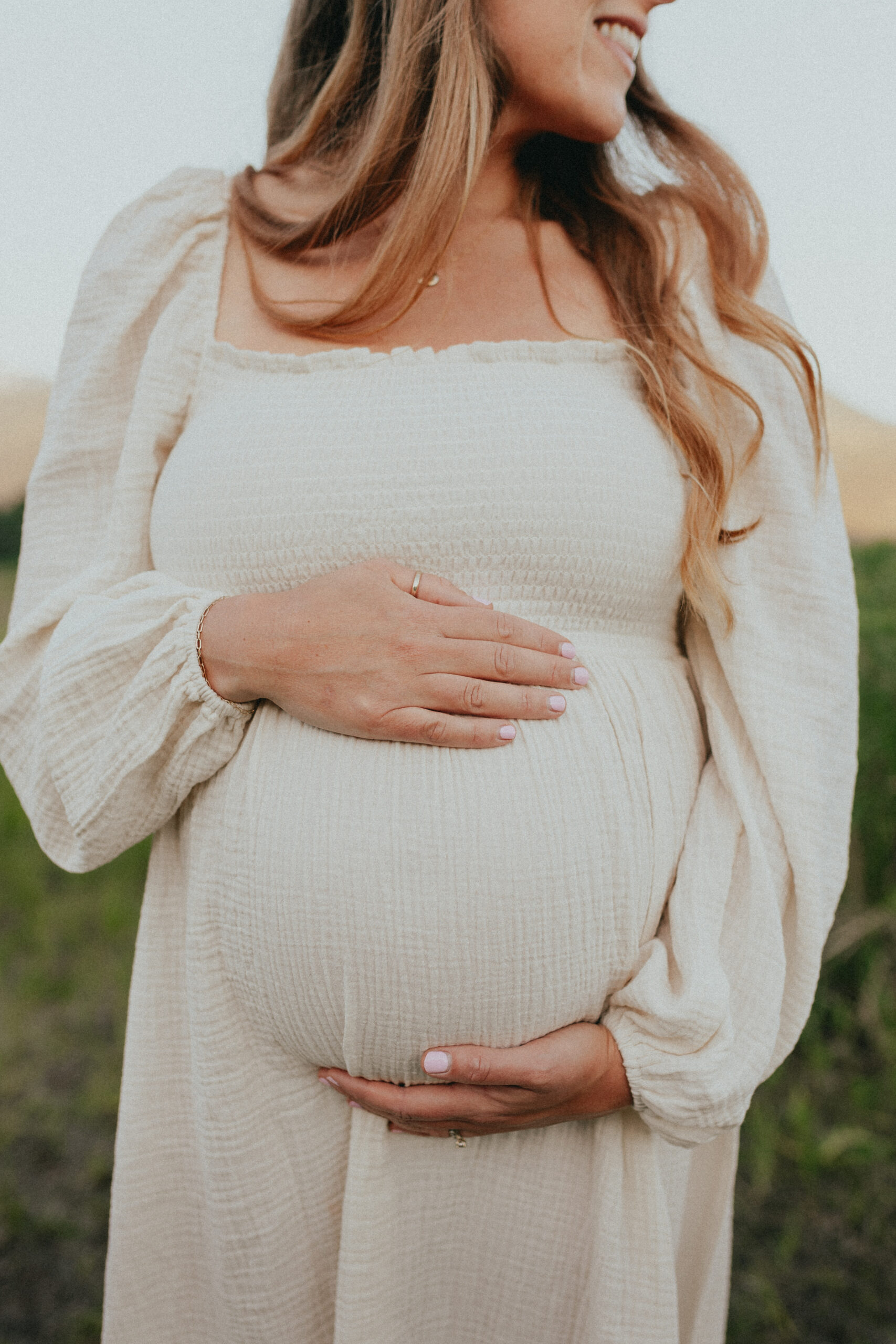 close up photo of a pregnant womans belly wearing a white dress while she cradles her bump