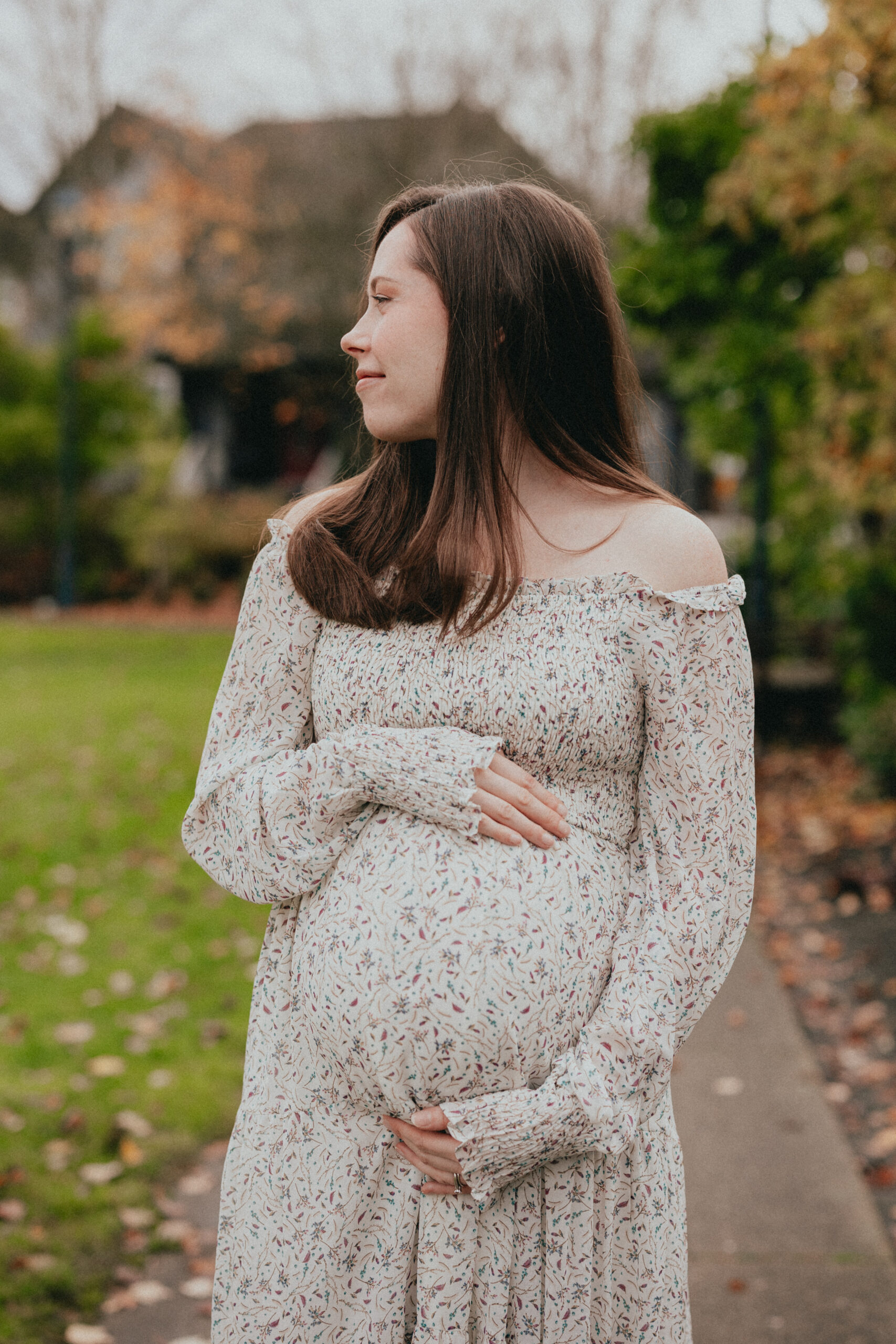 Photo of a pregnant woman holding her belly taken from the front while she looks to the side smiling to show maternity photoshoot dresses