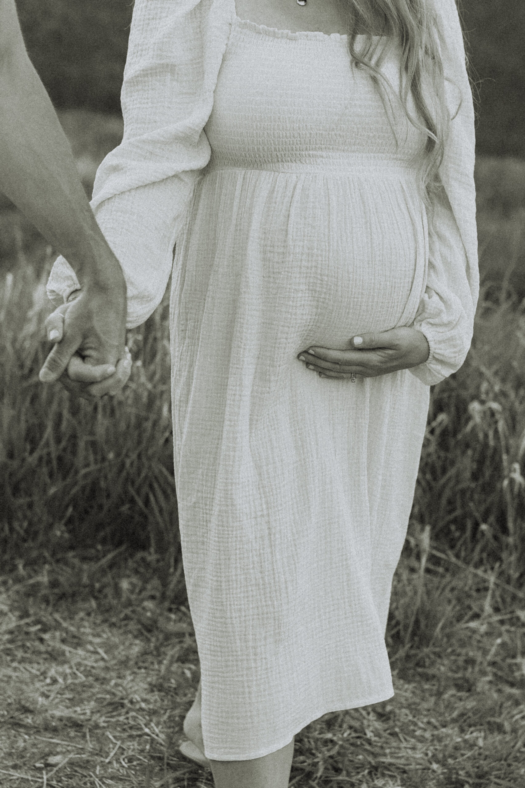 photo of a pregnant woman holding hands with her husband with the focus on her belly to show maternity photoshoot dresses