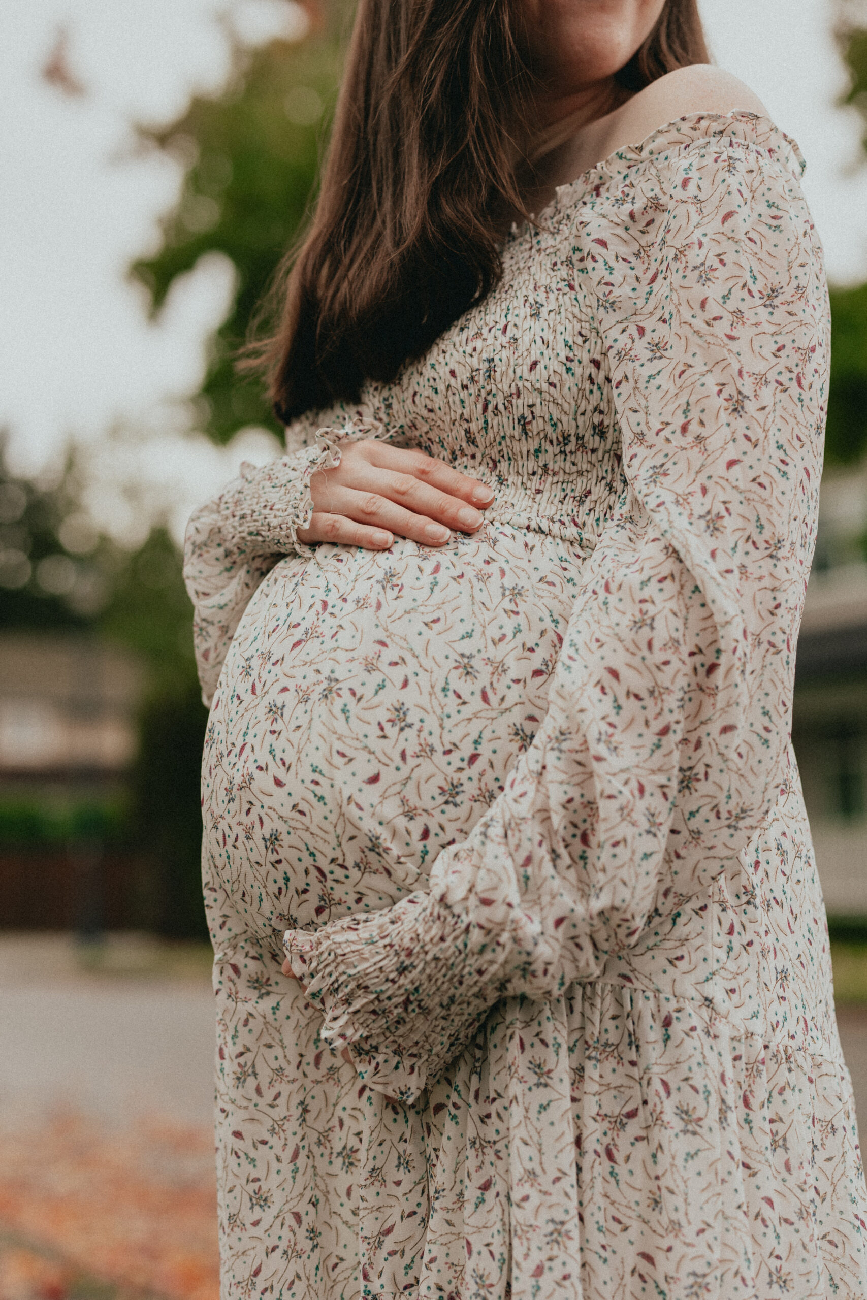 close up photo of a pregnant womans belly in a white and floral dress