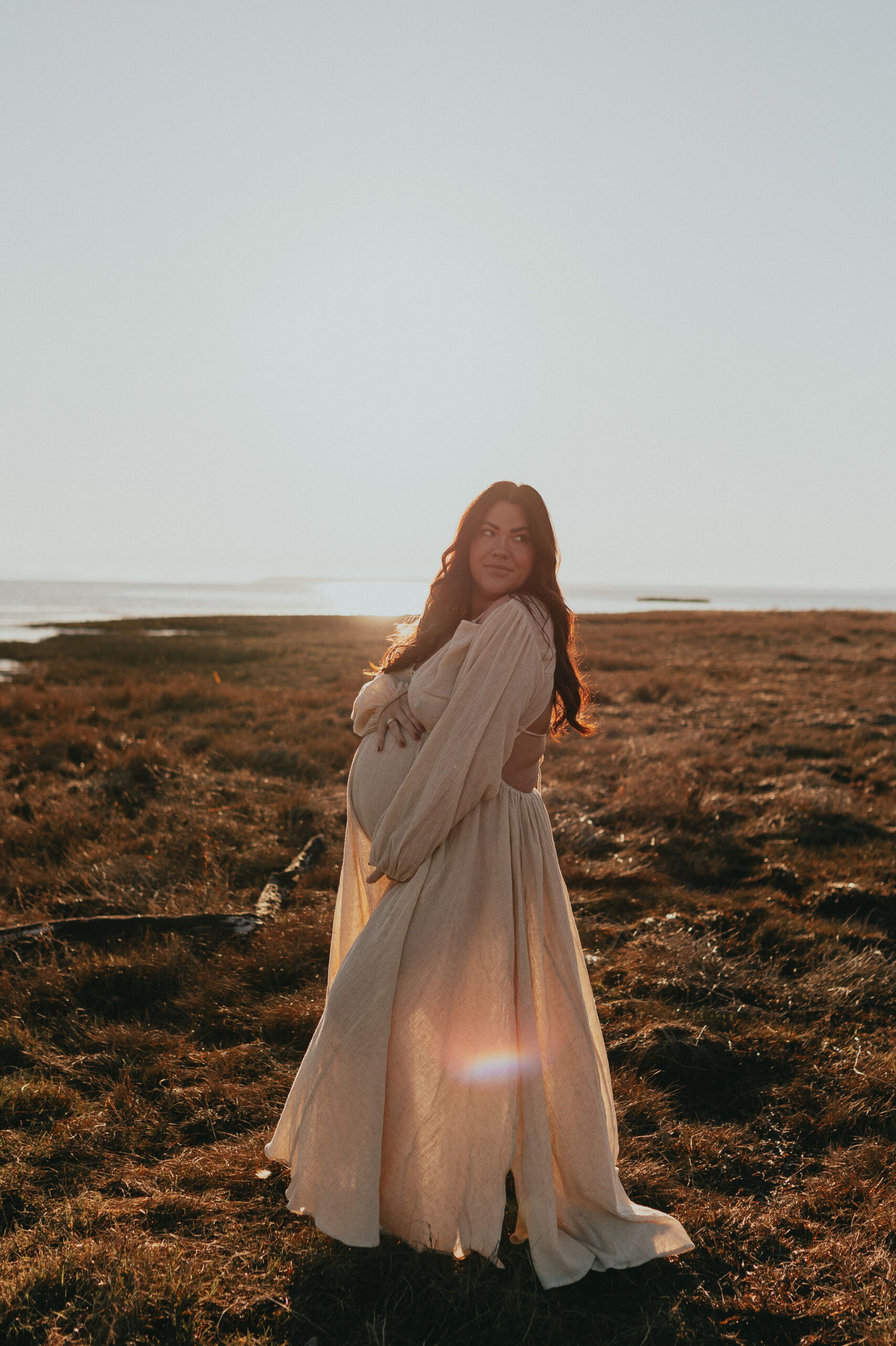 photo of a pregnant woman holding her belly looking at the camera on the beach for a blog about maternity photoshoot dresses