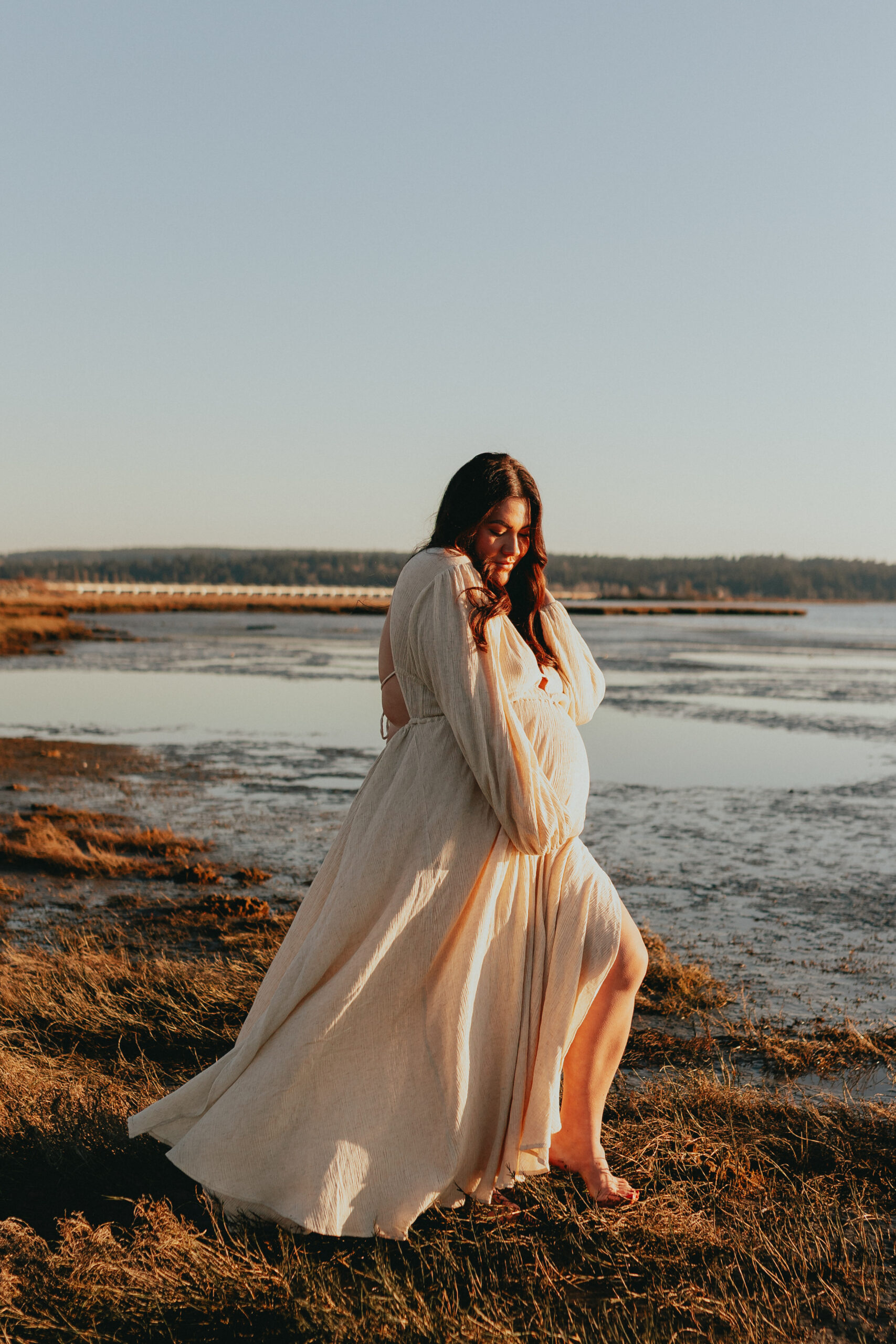 photo of a pregnant woman on the beaching walking towards the water while holding her bump for a blog about maternity photoshoot dresses