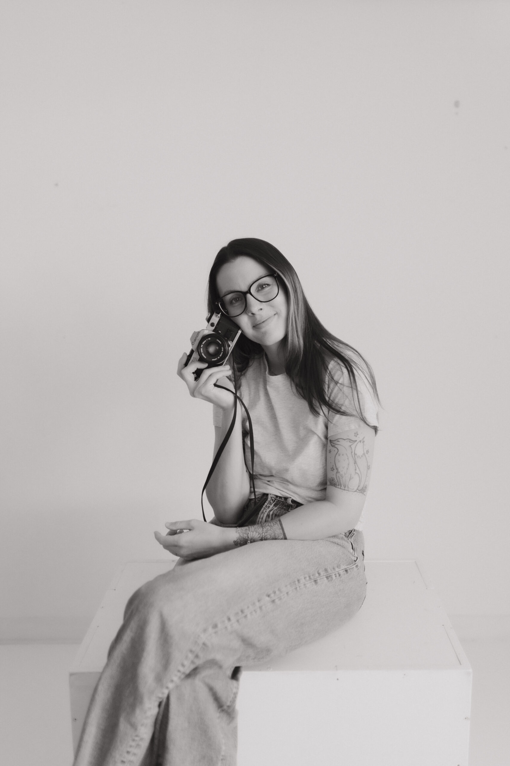 black and white photo of a newborn langley photographer where she is sitting on a table and holding a film camera near her face