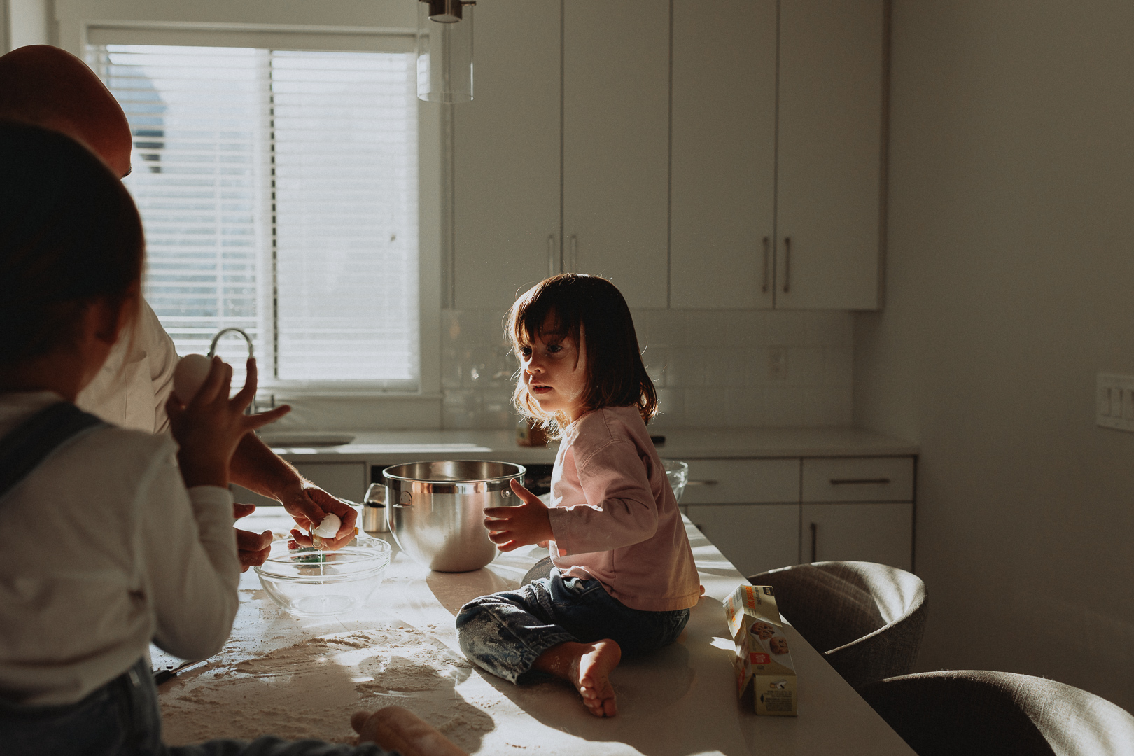 photo of a little girl sitting on a kitchen island while another girl and her dad bake cookies taken in langley