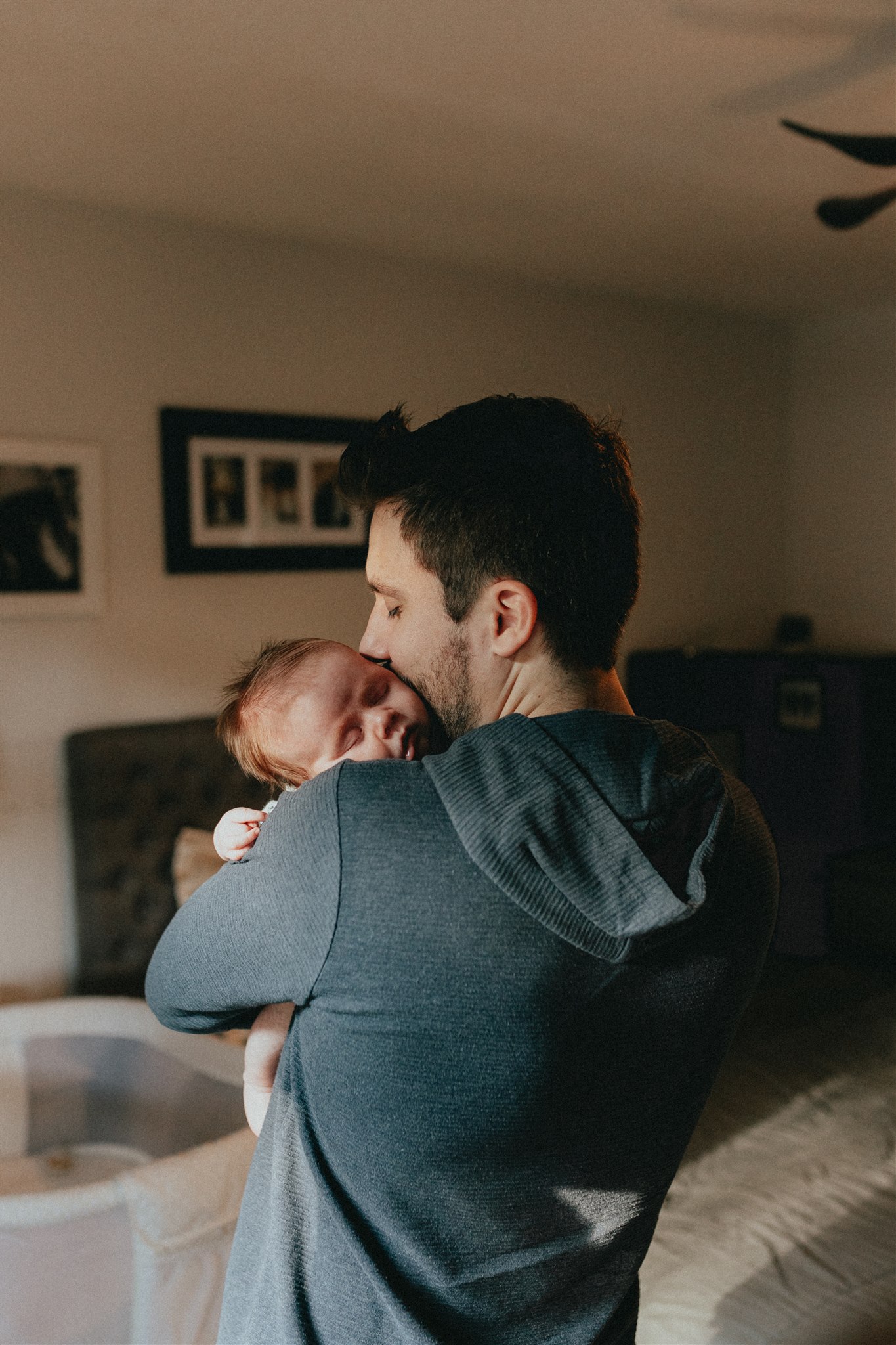 photo of a dad holding his newborn baby over his shoulder and kissing the sleeping baby on the head. Taken by a langley family & newborn photographer