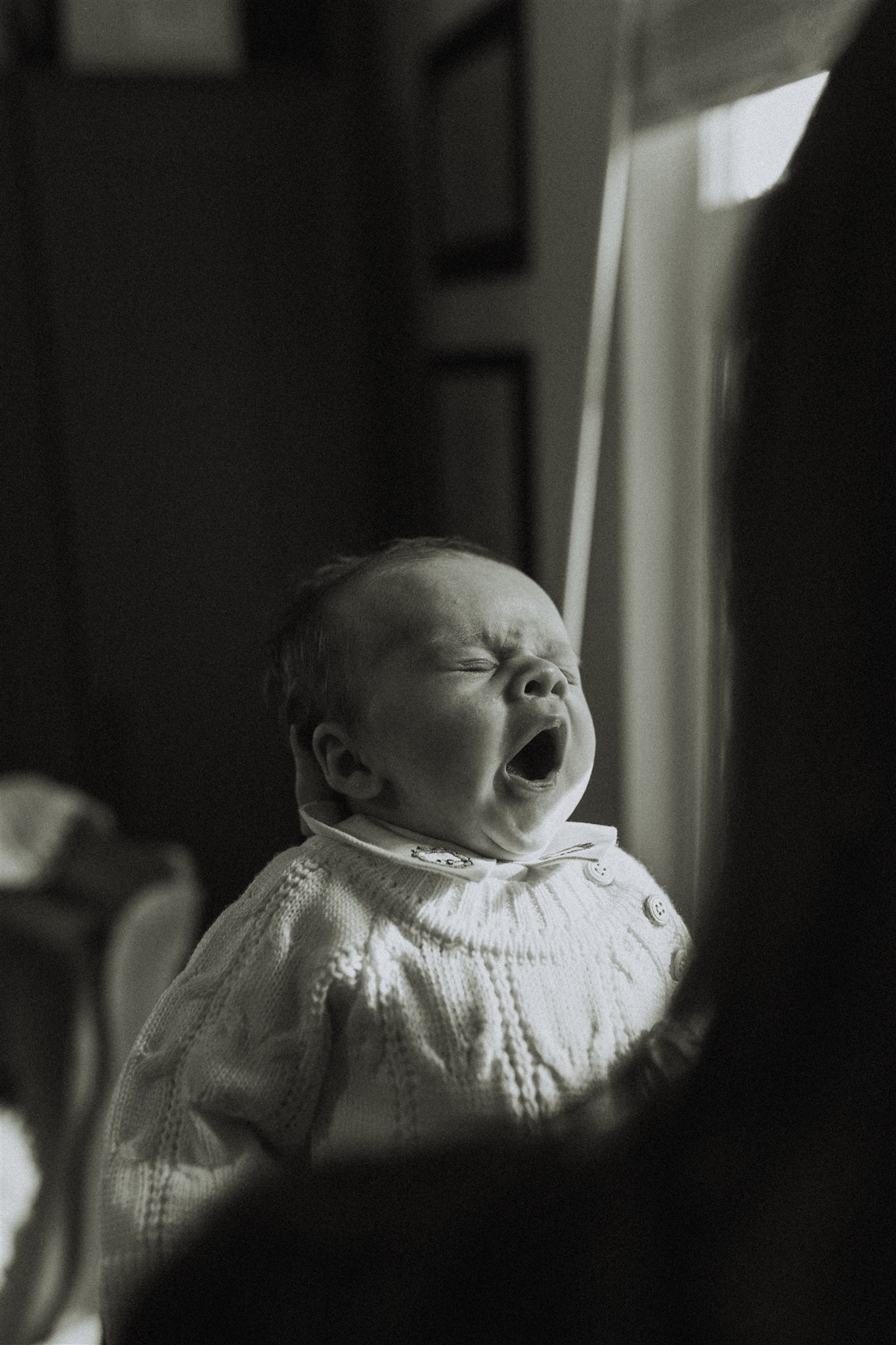 black and white photo of a baby yawning taken over moms shoulder while she is holding him. 