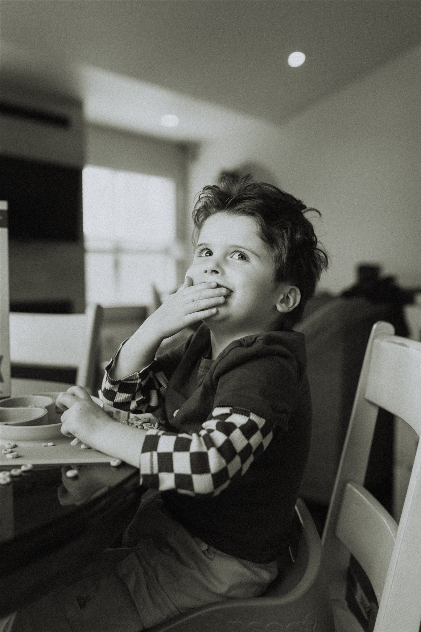 black and white photo of a little boy smiling at the camera while putting cheerios in his mouth taken in langley