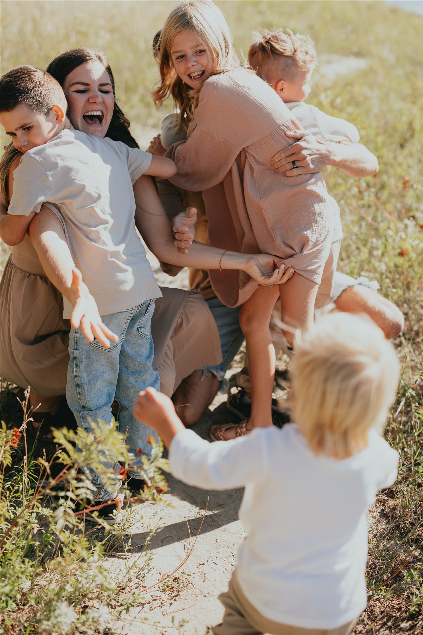 Photo of a family of 5 all hugging and laughing with a toddler running towards them wanting a hug too. Taken by a langley family & newborn photographer