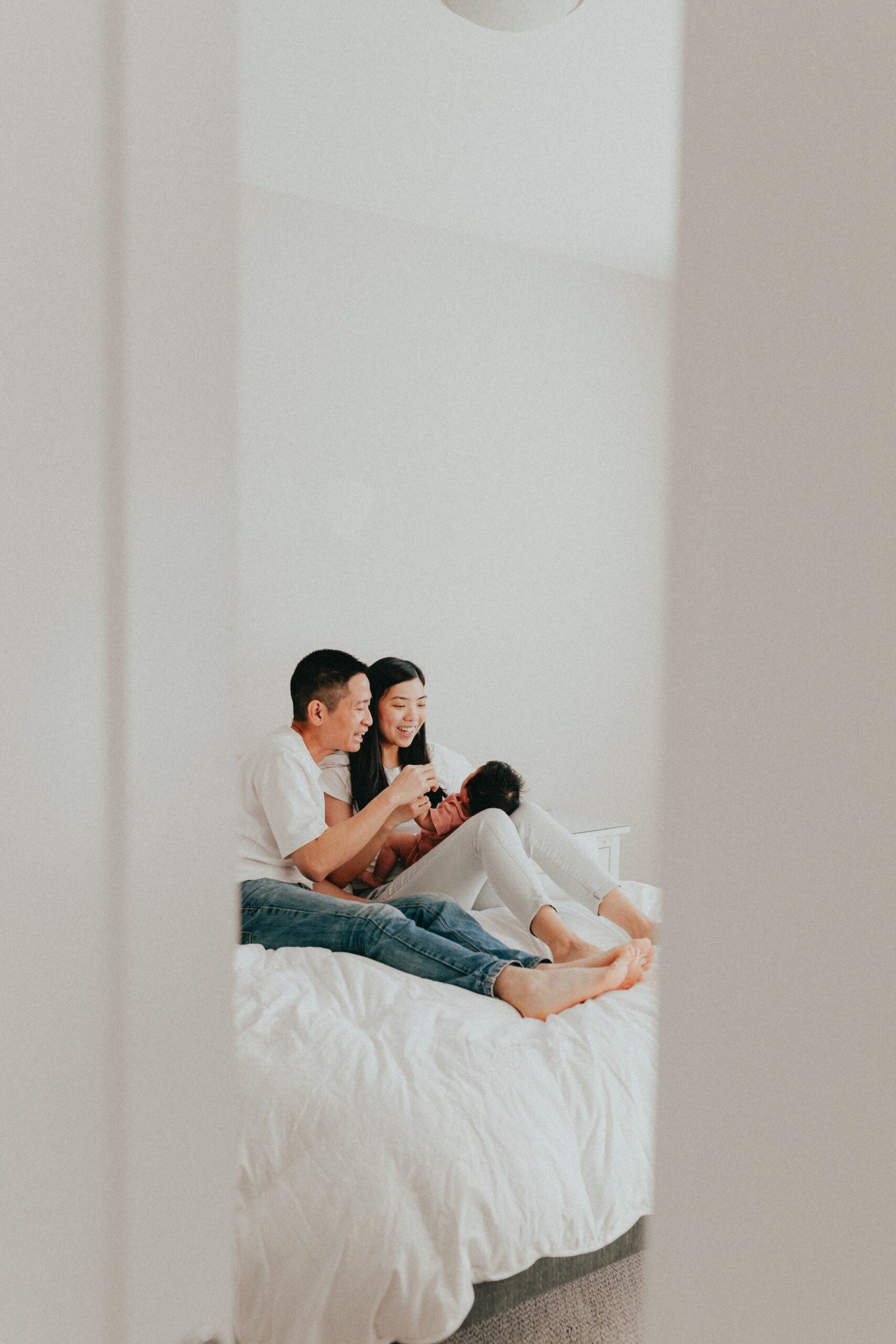 photo of a mom and dad smiling and talking to their newborn baby while sitting on the bed taken from outside of the room