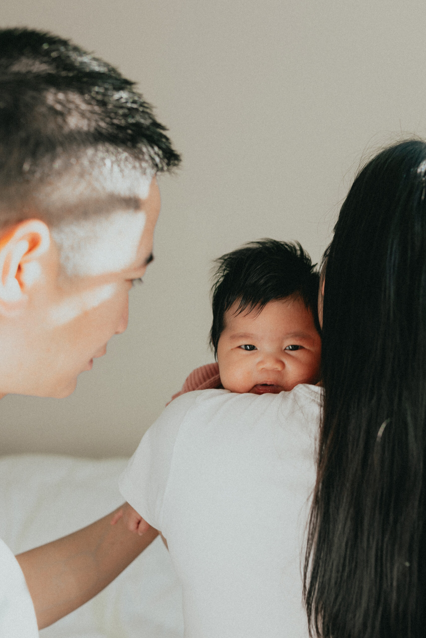 photo of a baby taken over moms shoulder while dad is patting baby on the back, out of focus in the image