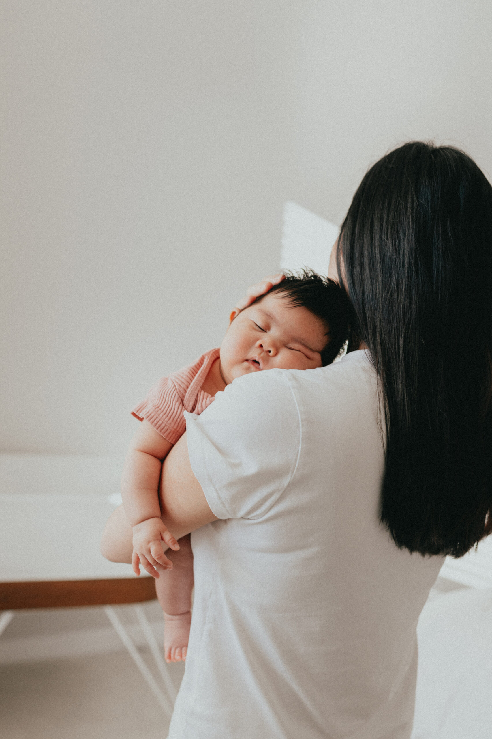 Photo of a baby sleeping on moms shoulder, taken from behind so you can see the babies face but not moms. Taken by a langley newborn photographer