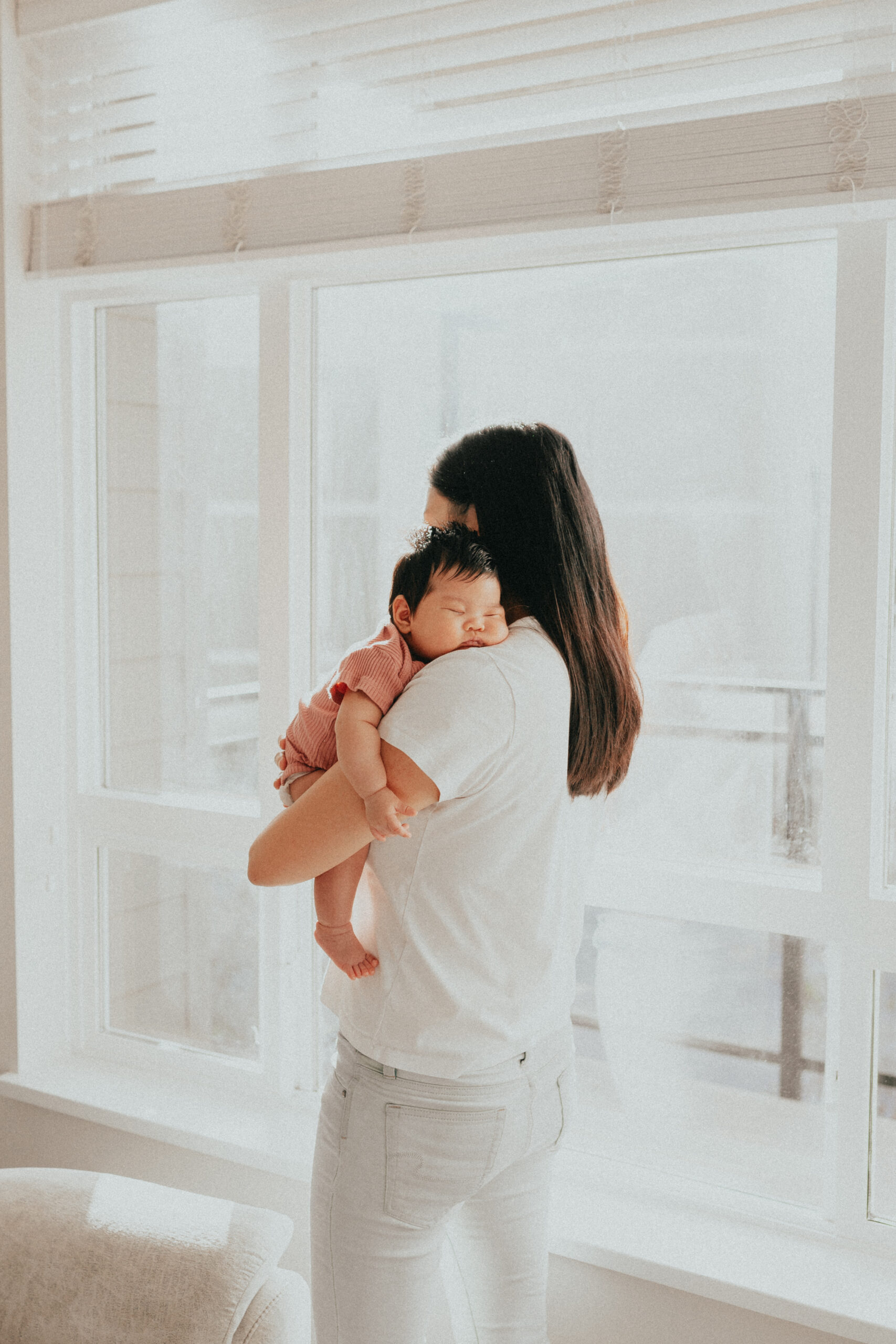 photo of a baby sleeping on her moms shoulder while mom looks out of the window. taken by a langley newborn photographer