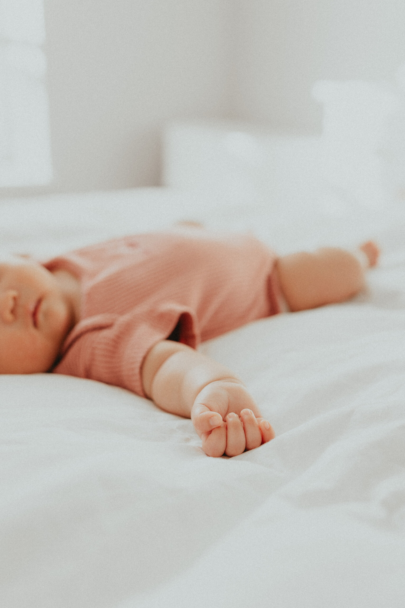 photo of a baby laying on the bed with the focus being on the baby's little tiny hand 