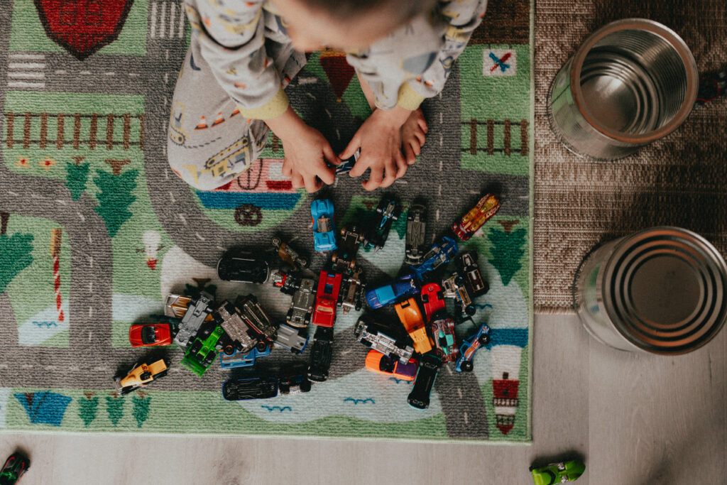 photo taken from above of a little boy sitting on a car mat with his hot wheels cars surrounding him on the floor