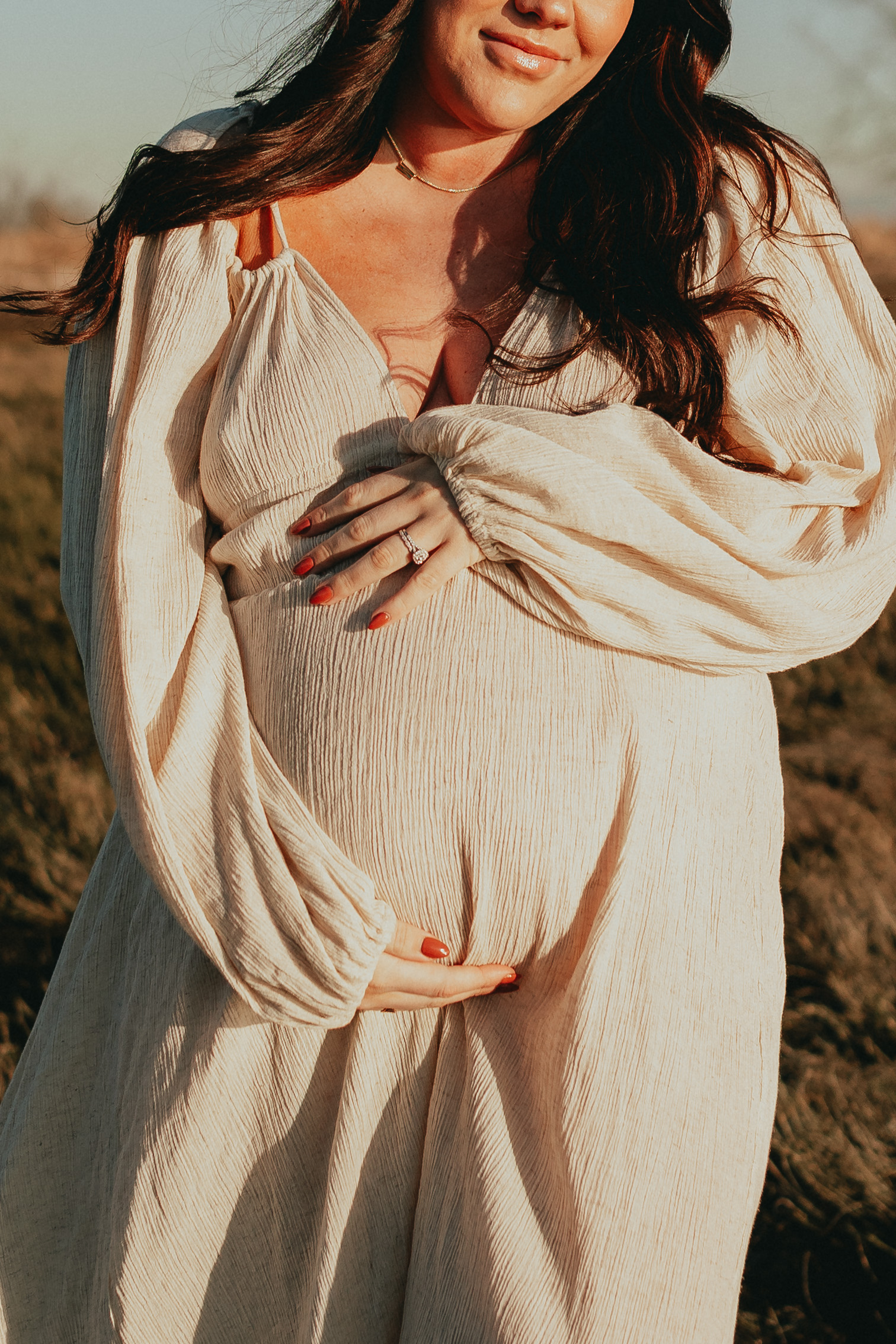 Photo of a pregnant woman holding her baby bump wearing a beige dress with the focus of the photo of the baby bump