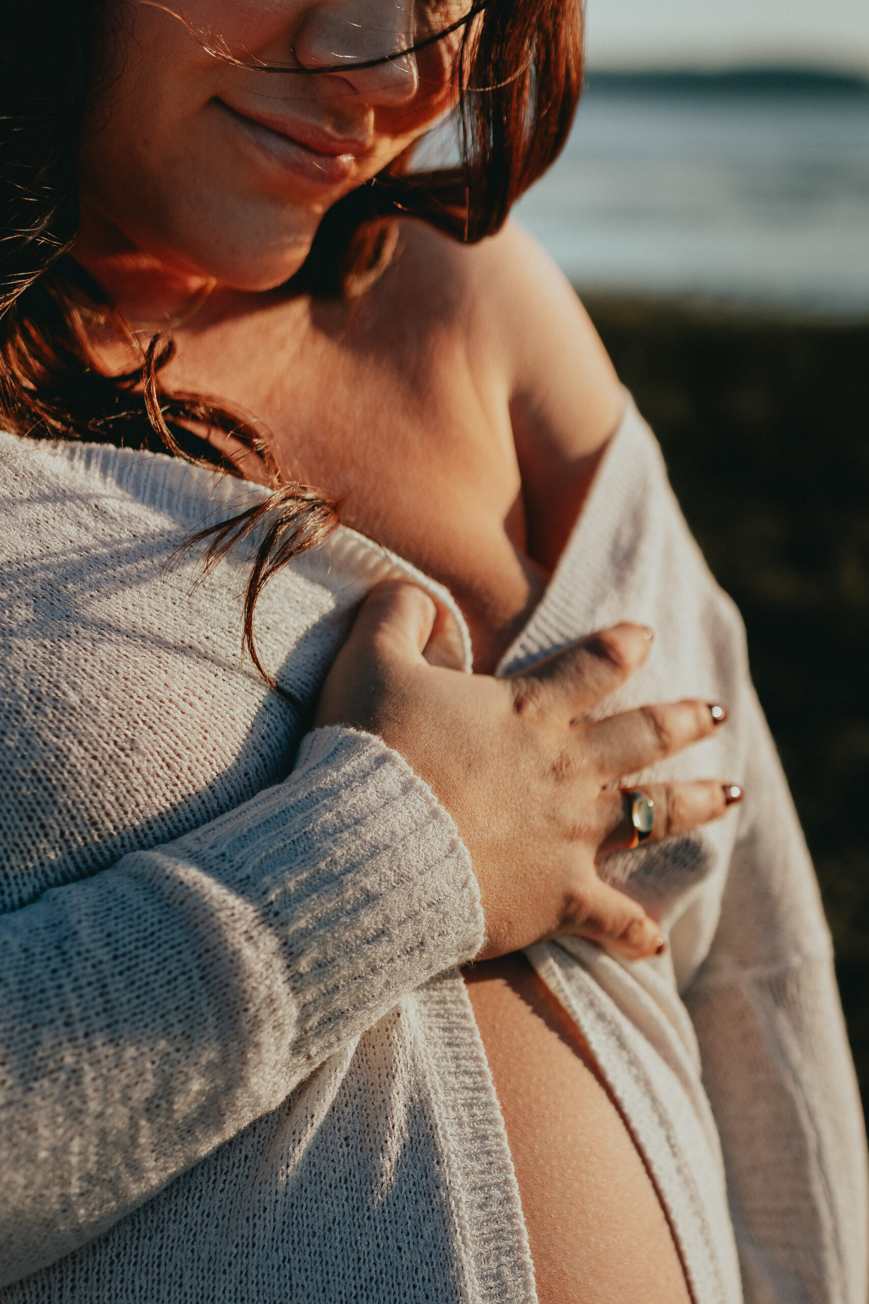 close up photo of a pregnant woman holding her sweater over her baby bump and you can barley see her smiling down at her bump