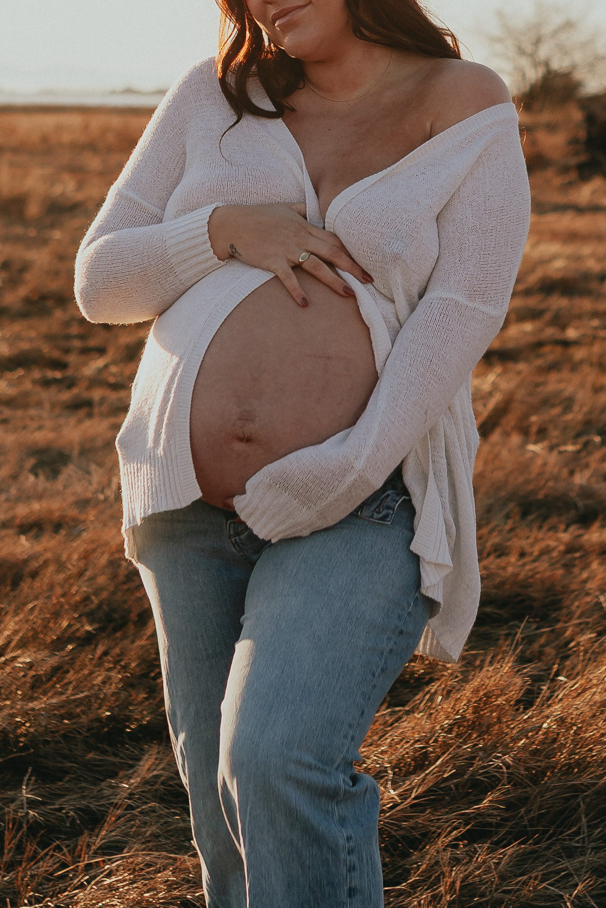 Photo of a pregnant woman holding her baby bump where you can only see her belly and the bottom of her smile taken by a vancouver maternity photographer