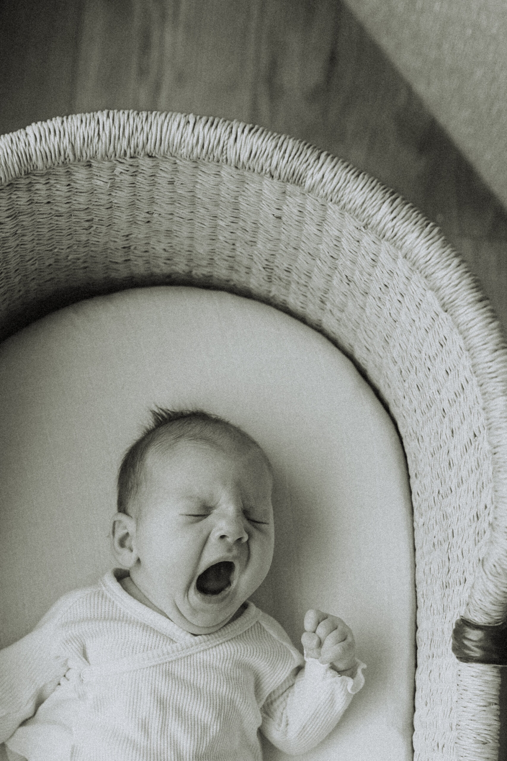Black and white photo of a baby laying in their bassinet yawning