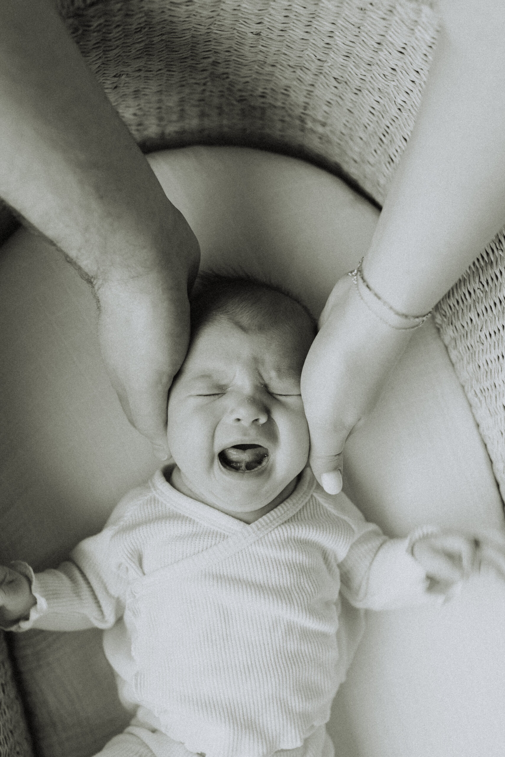 black and white photo of a baby in their bassinet with mom and dad each holding a side of her head