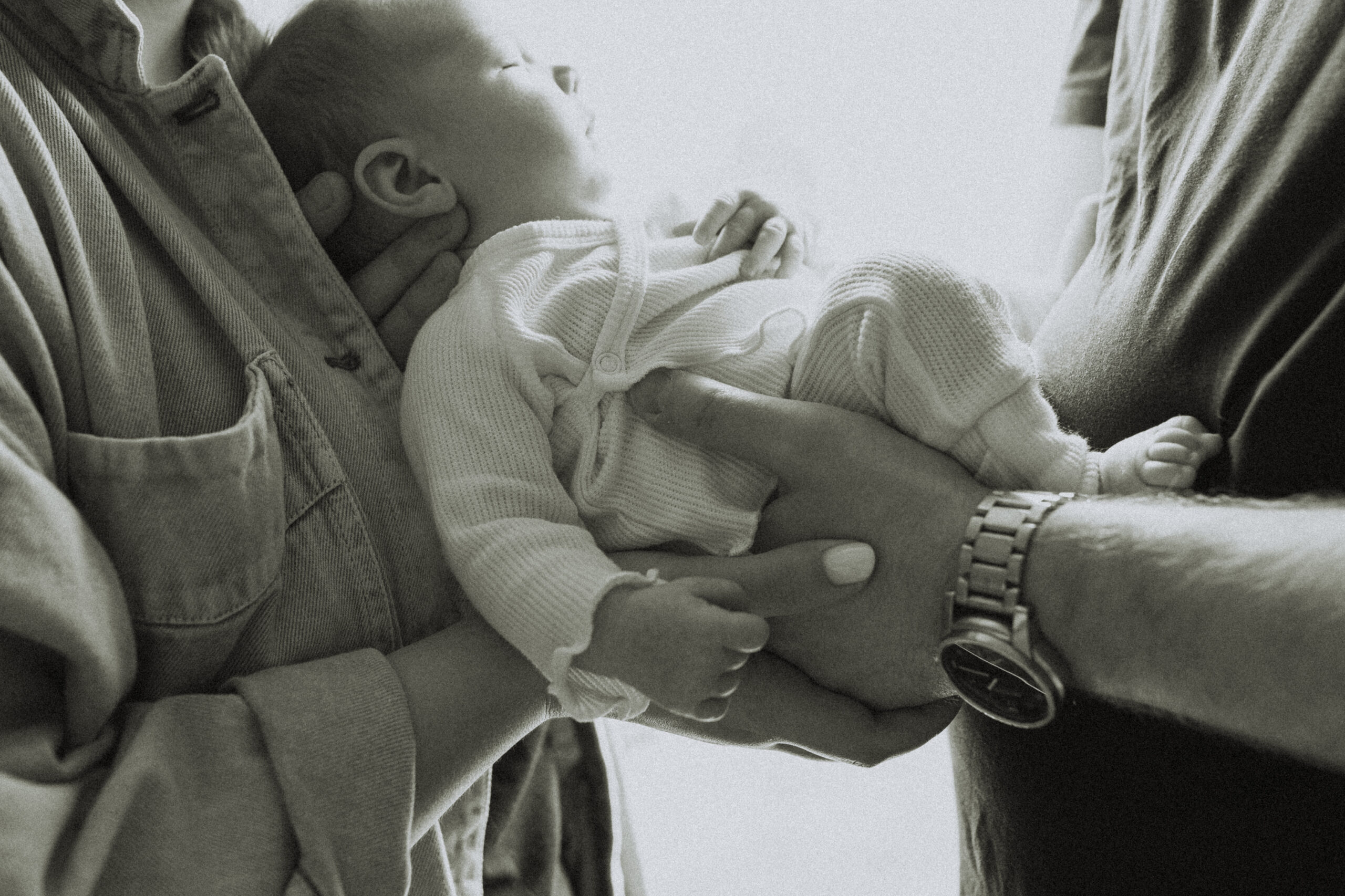 Black and white photo of a mom and dad facing eachother and holding their baby in between them while the baby is sleeping