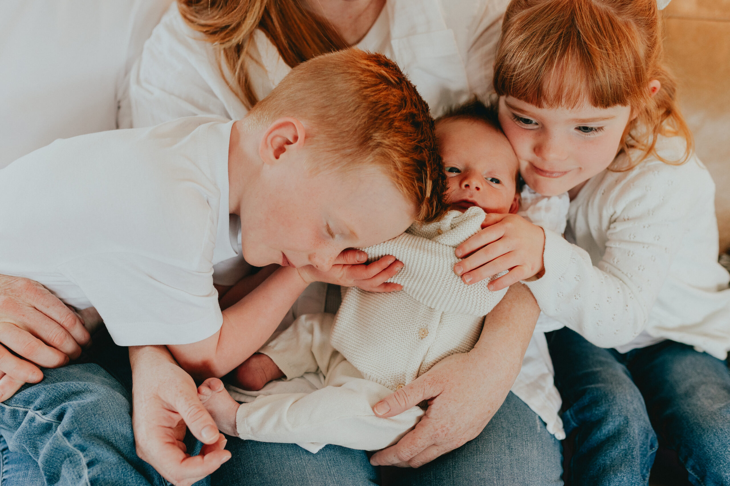 Photo of a mom holding a newborn baby while the older brother and sister snuggle close.