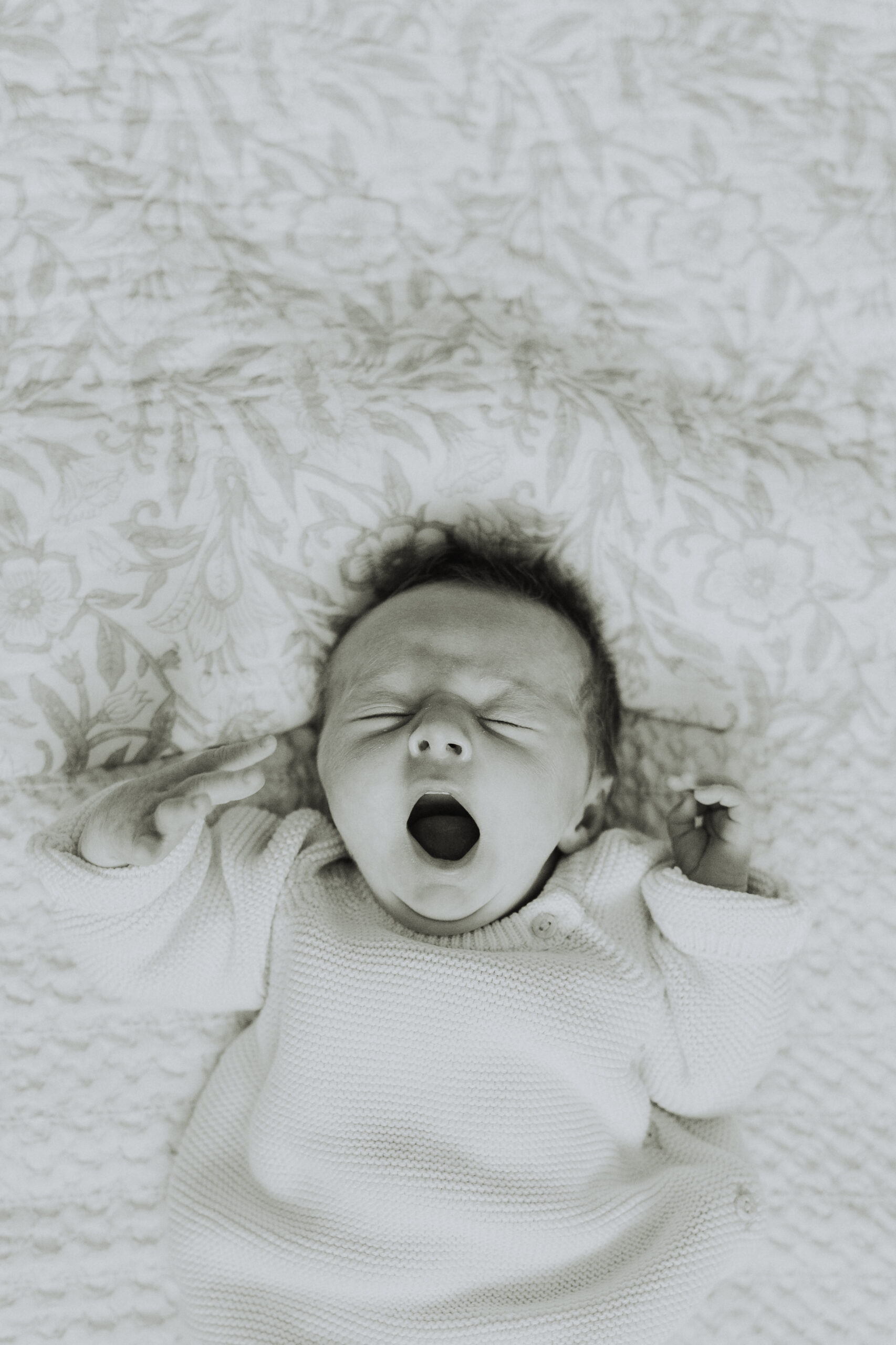 Black and white photo of a baby laying on a big bed yawning