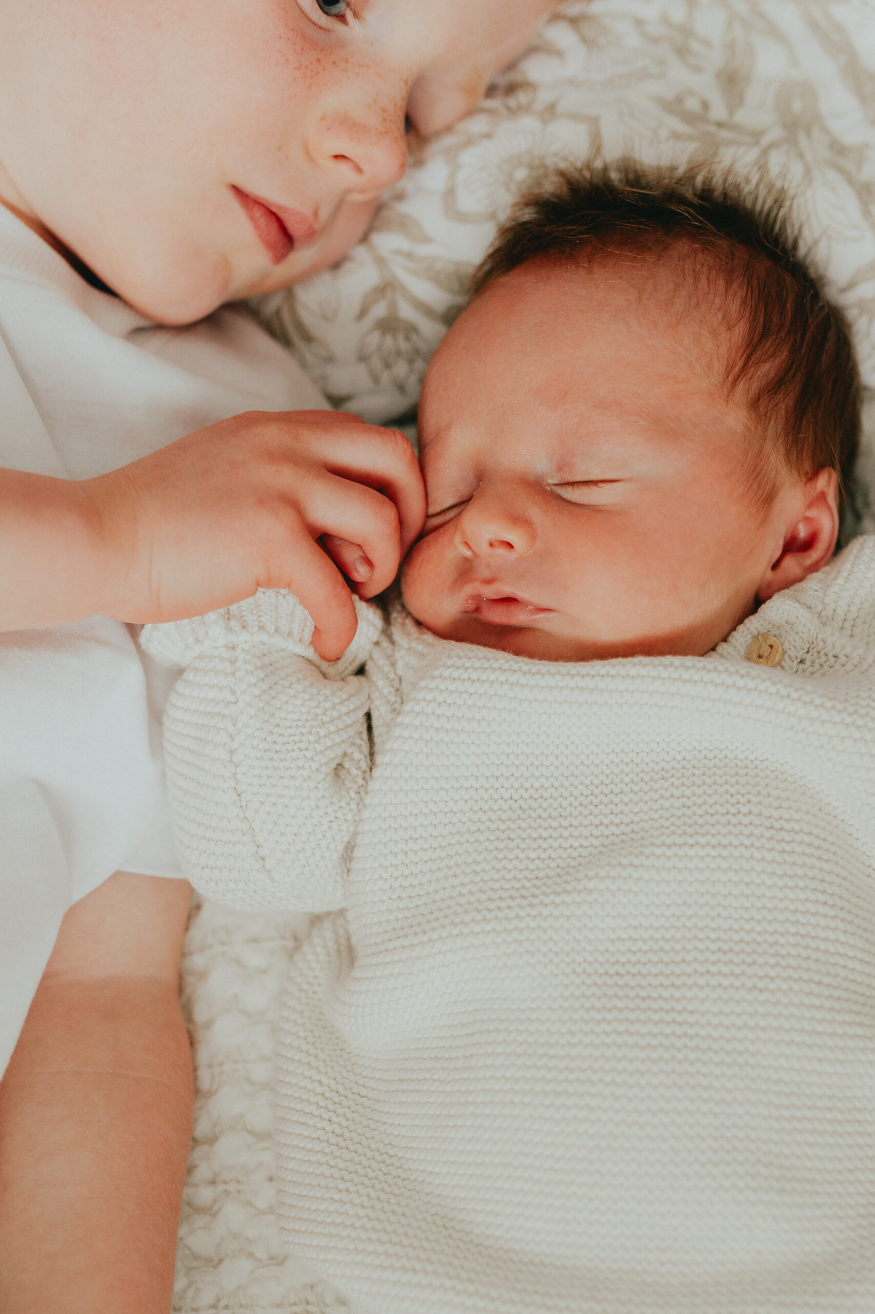 Close up photo of a big brother holding his baby bothers hand while the baby sleeps