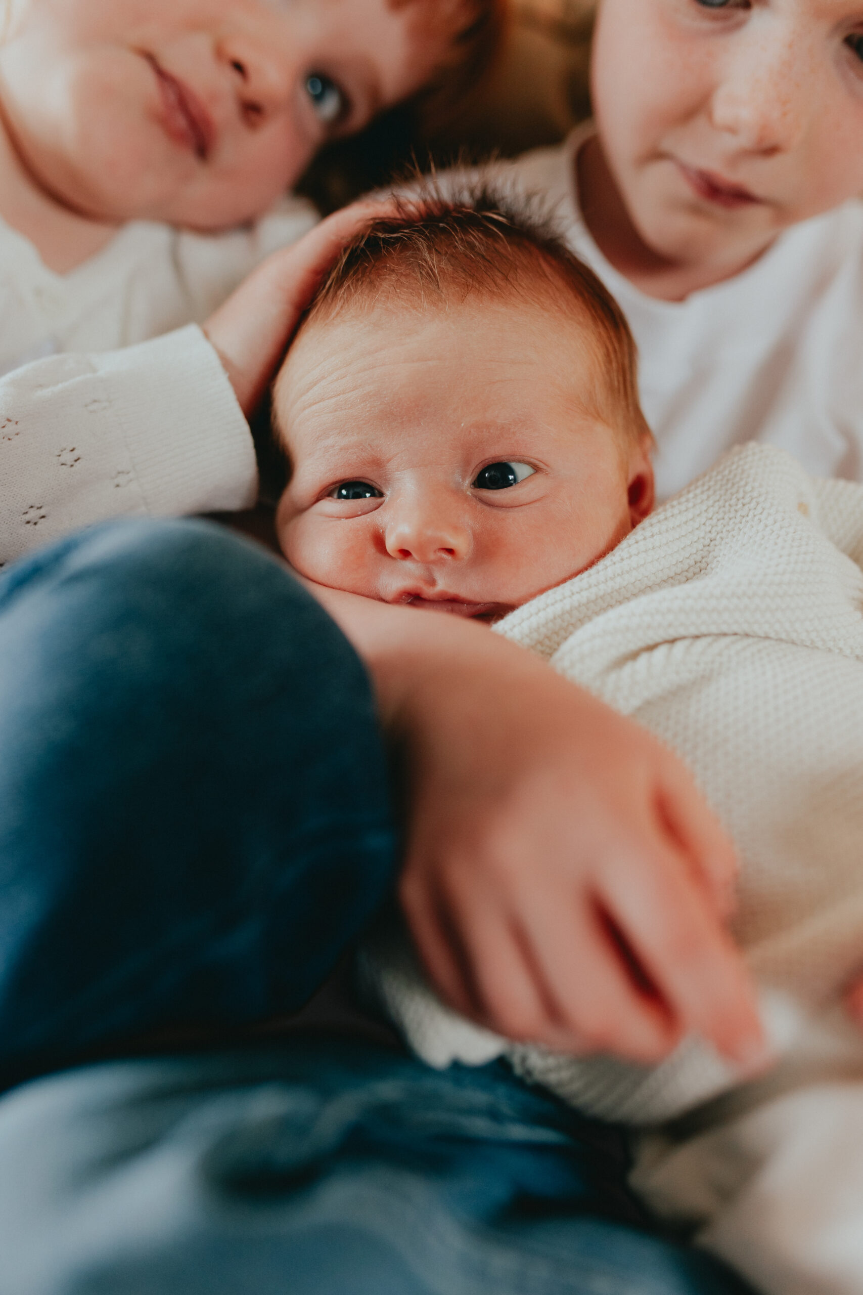 Photo of a newborn baby being squished between his older siblings