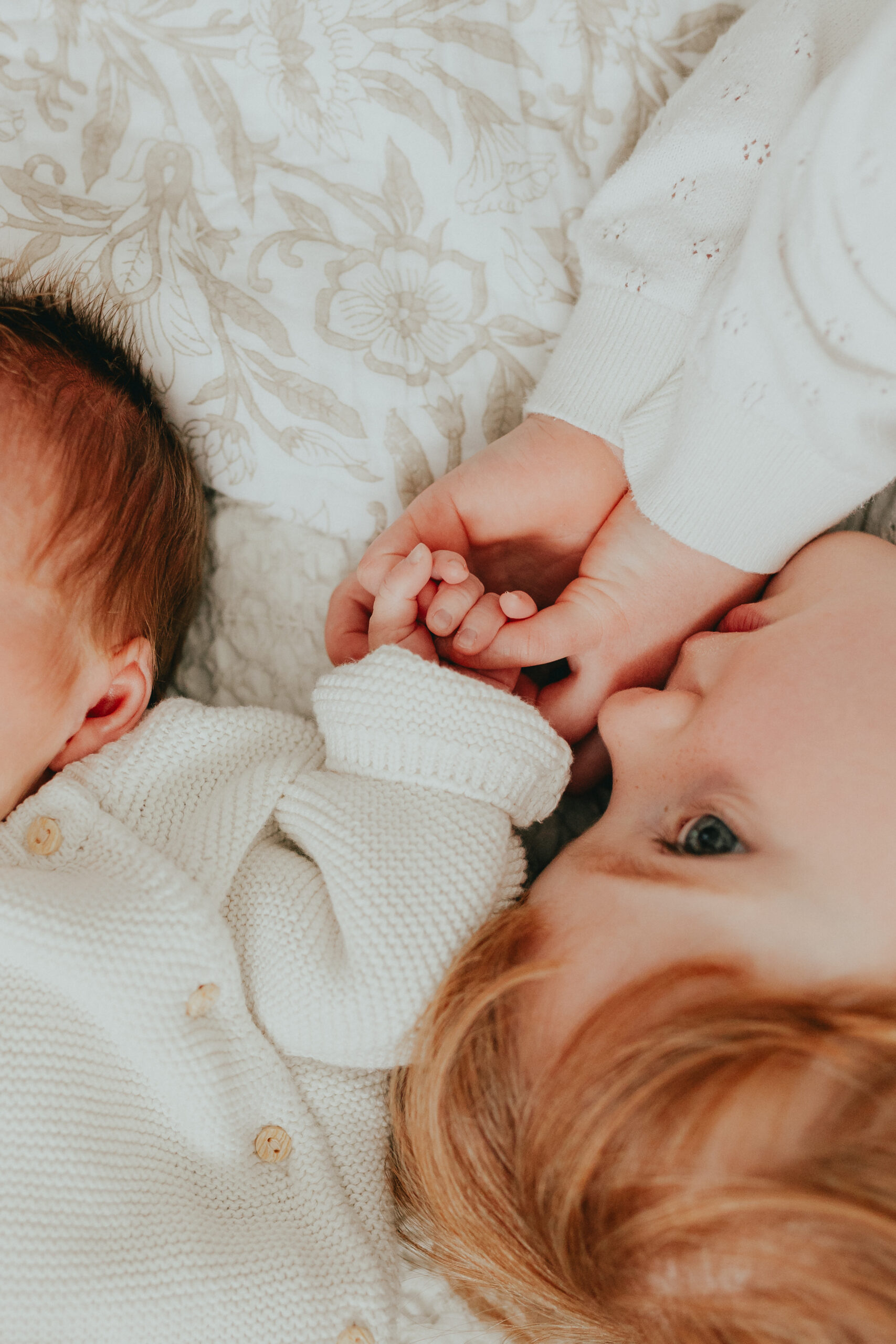 Close up photo of a big sister holding her baby brother's hand taken for the newborn family photos