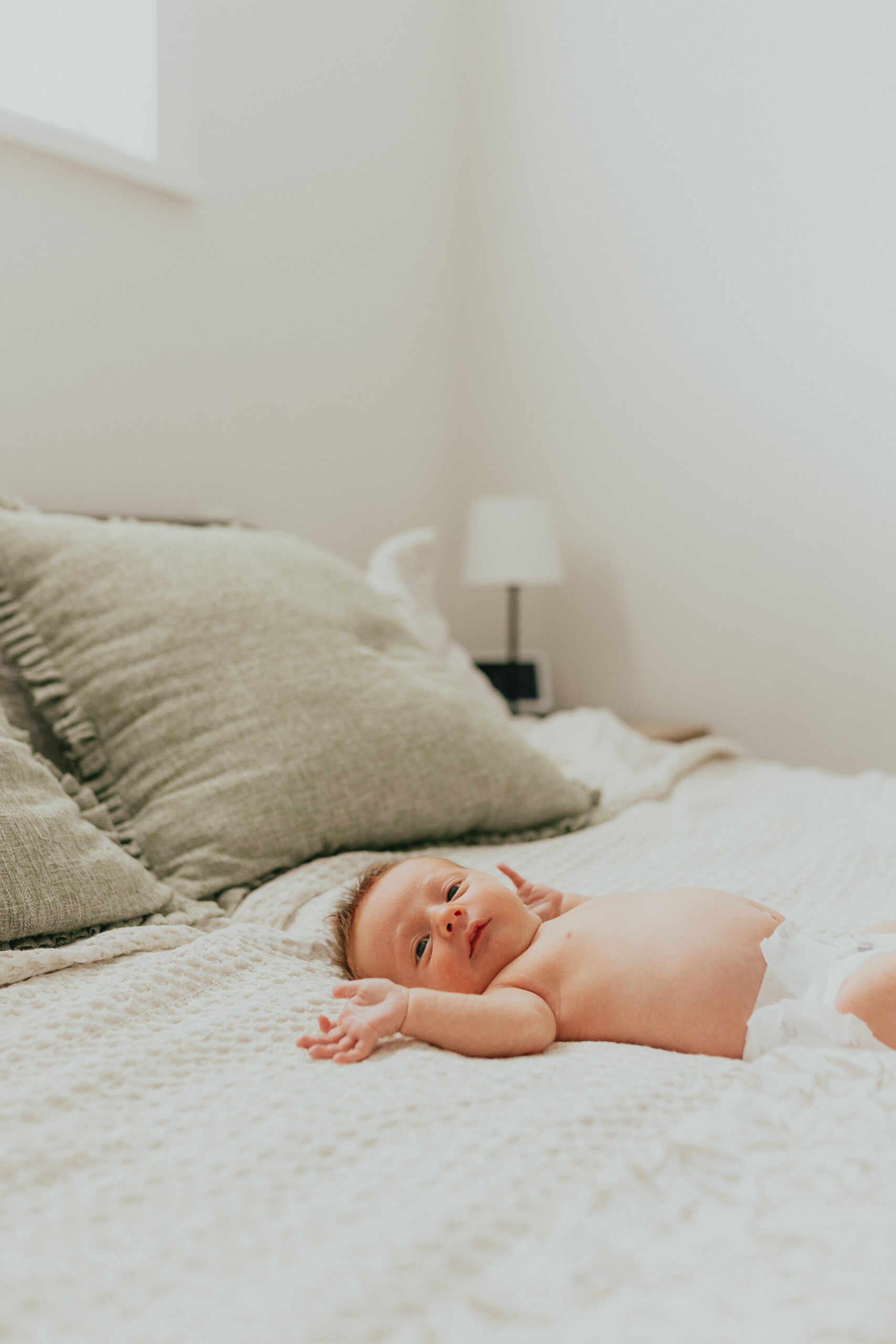 Photo of a newborn baby laying on the big bed in just a diaper looking to the side taken for newborn family photos
