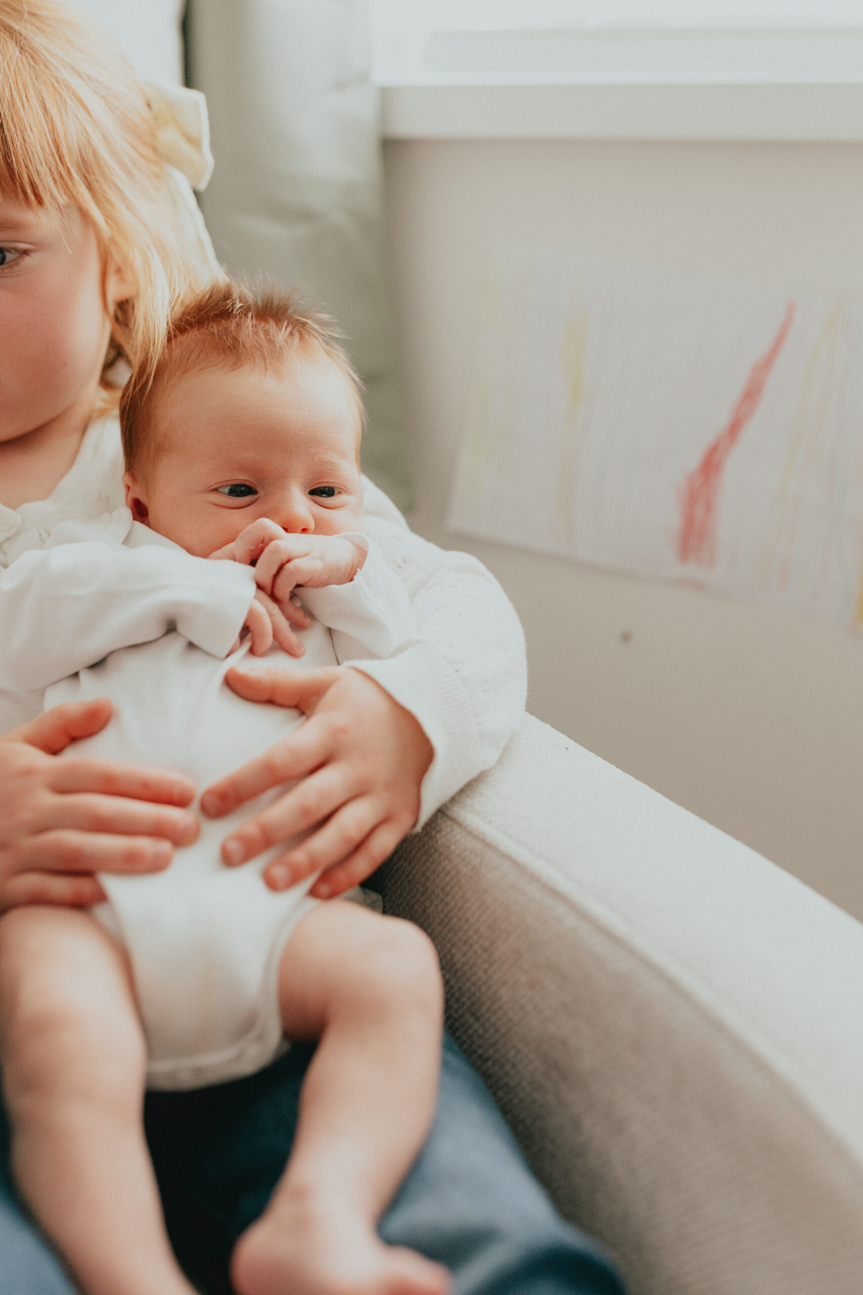 Photo of a big sister holding her baby brother while sitting on the nursery chair