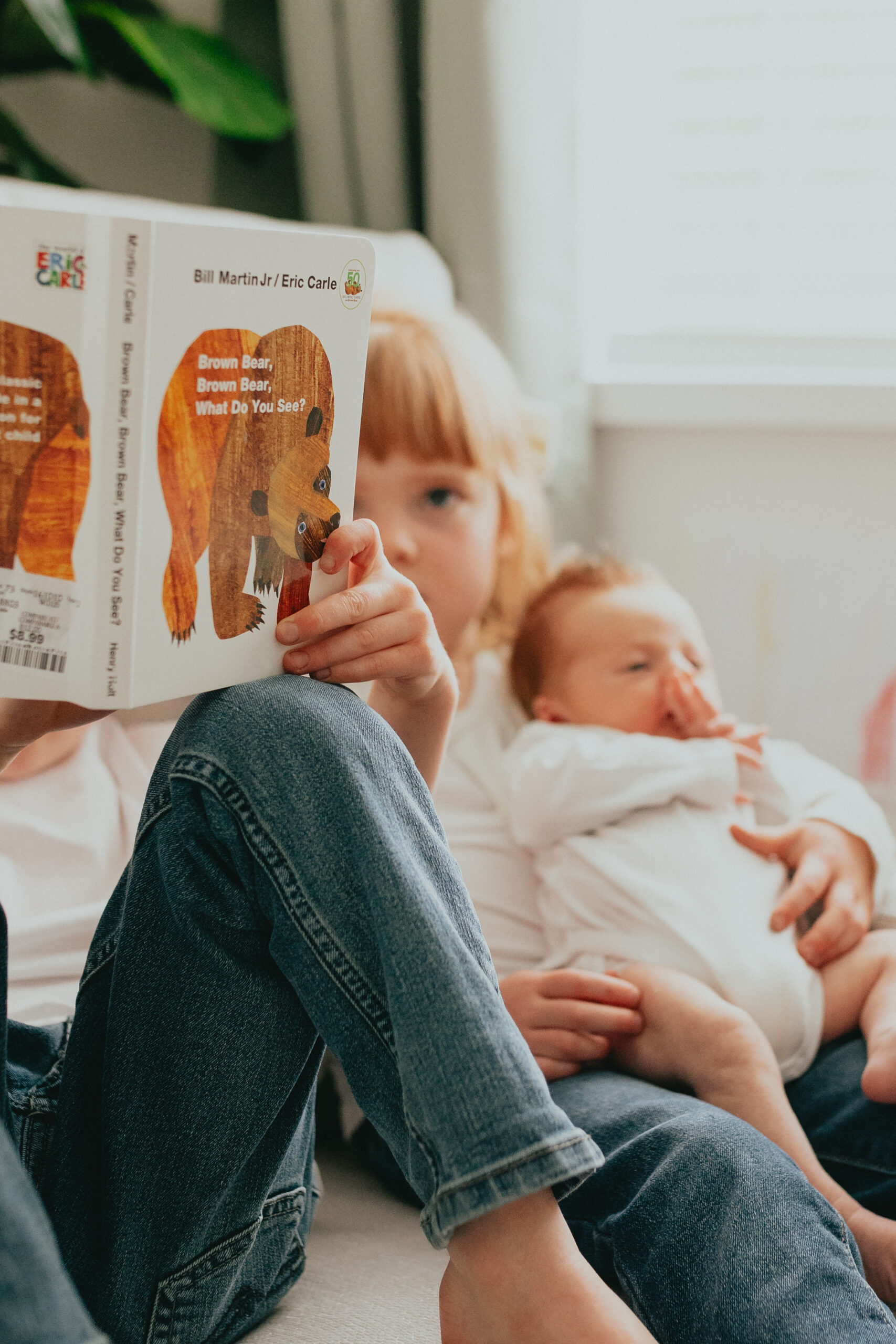 Close up photo of a big brother reading to his younger siblings the book "brown bear brown bear" taken for newborn family photos