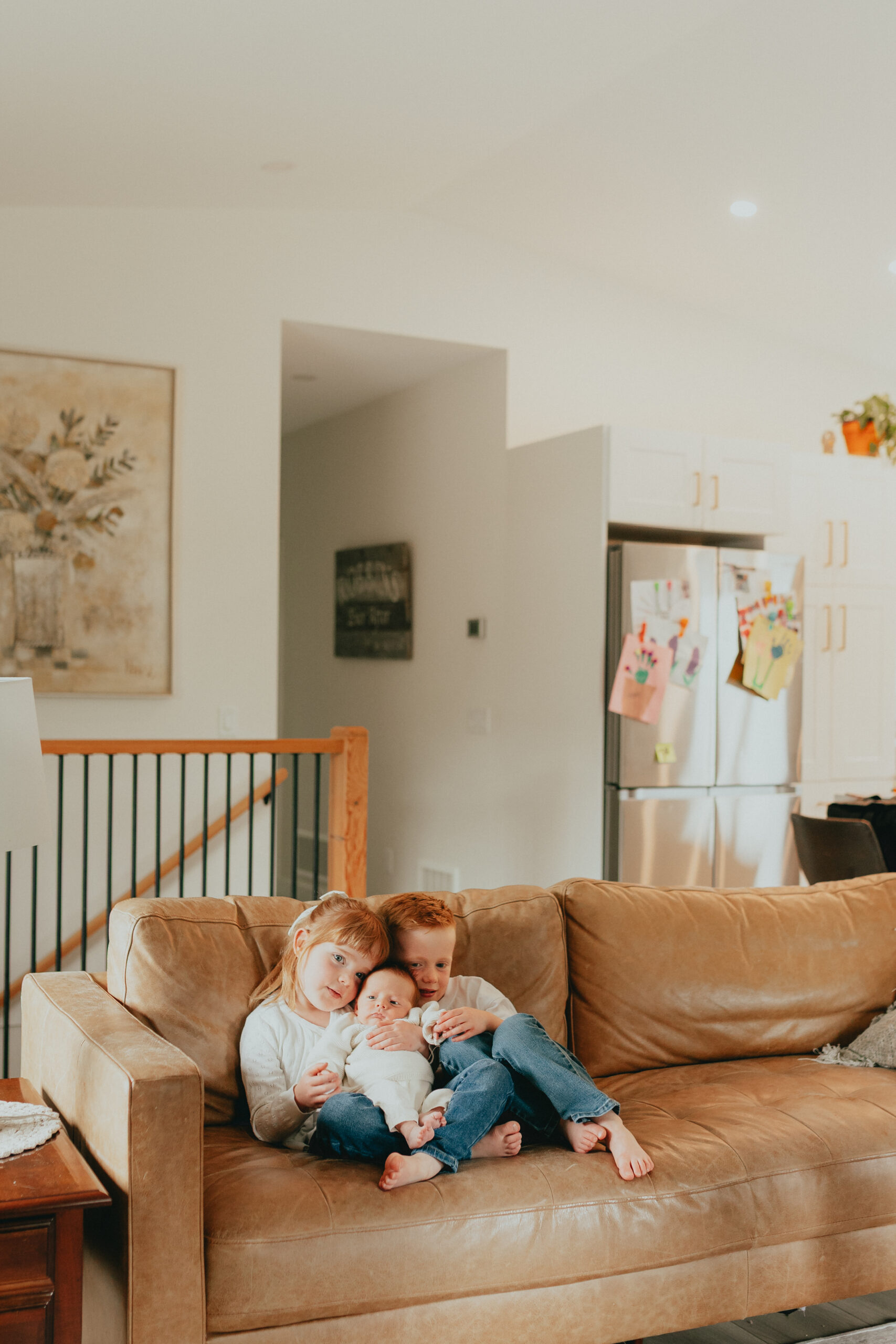 Photo of an older brother and sister holding their newborn baby brother sitting on the couch