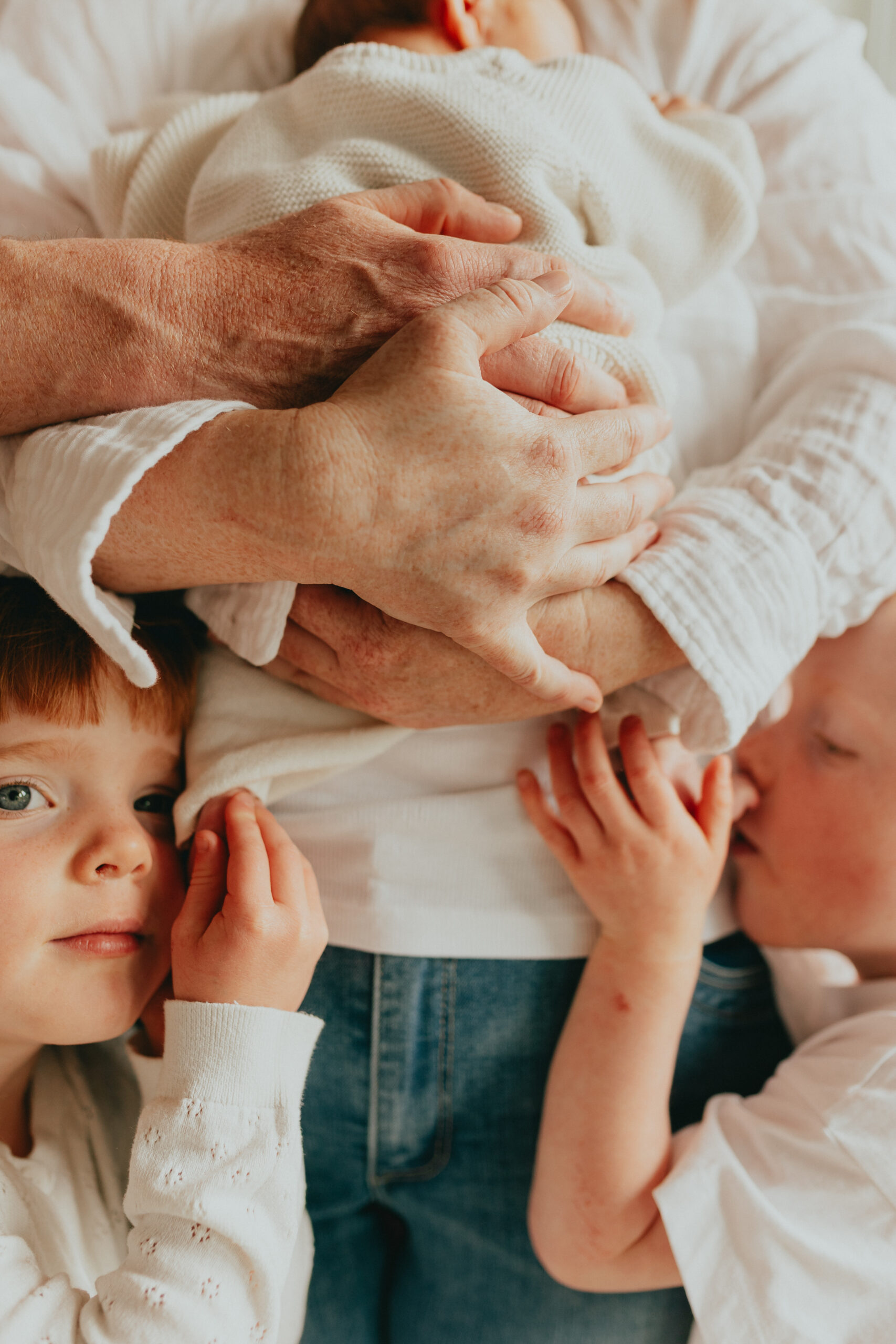 Close up detail photo of mom and dad cradling their newborn baby while younger brother and sister hold onto baby's feet