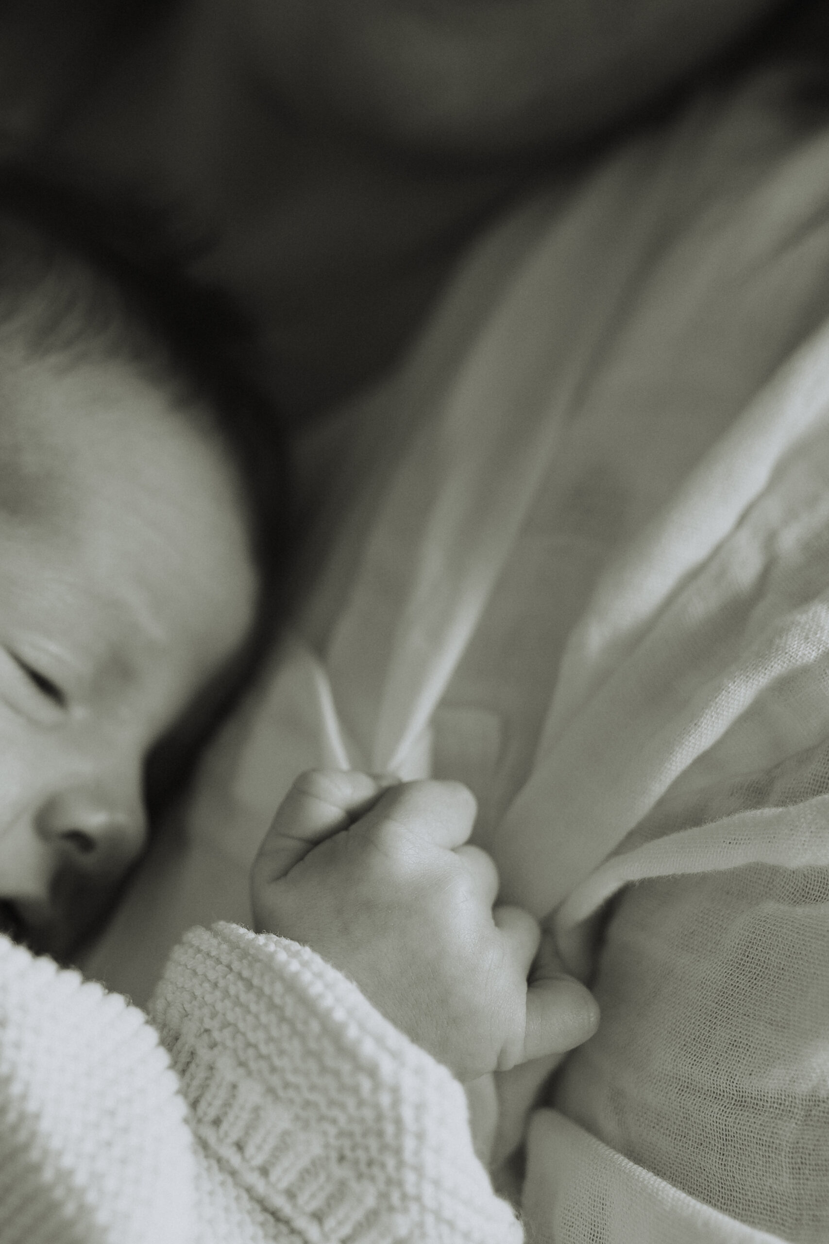 Black and white photo of a mom holding her newborn baby while the baby is holding onto moms shirt