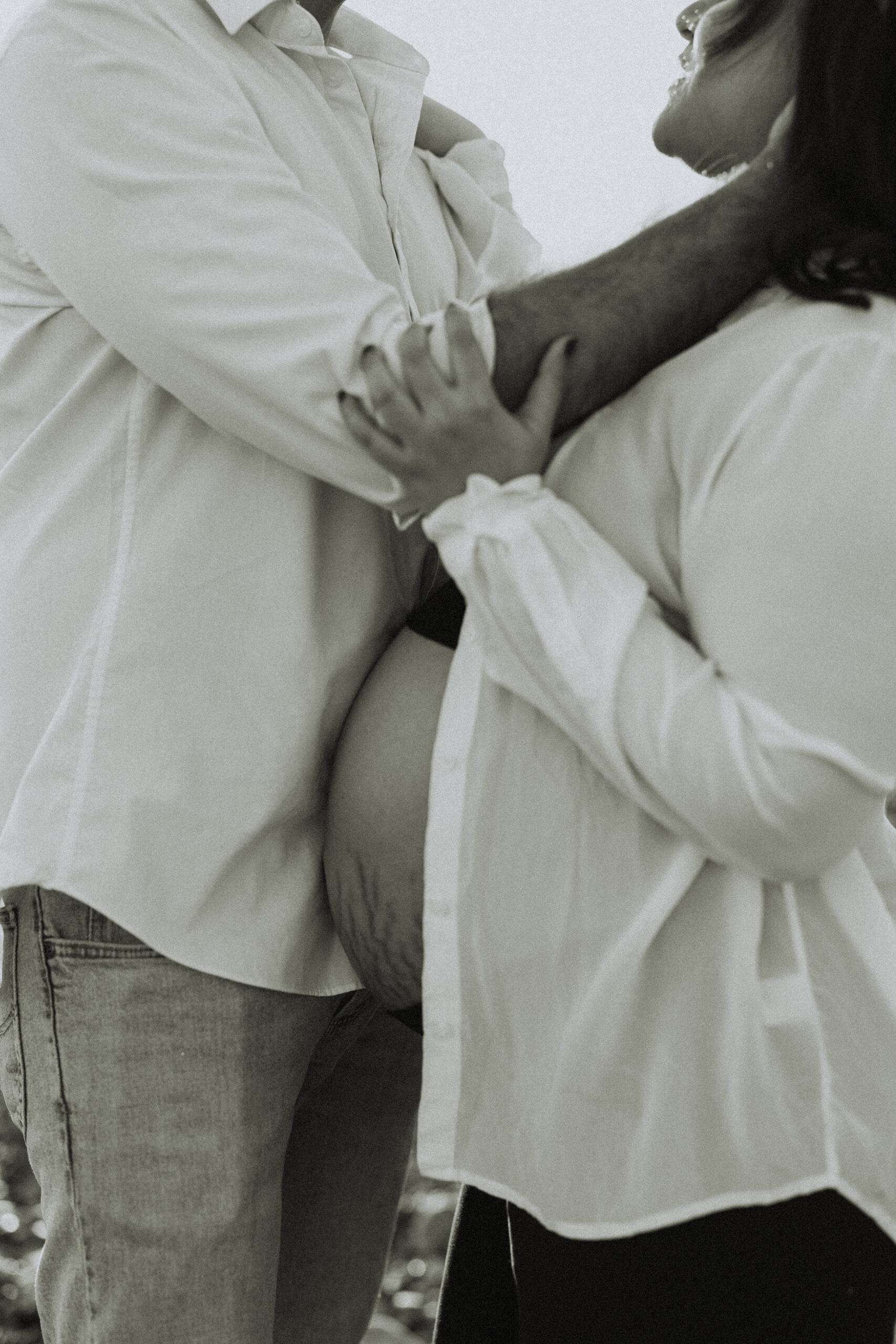 Black and white close up photo of a husband and wife hugging where you can only see the pregnant womans bump and the husbands torso