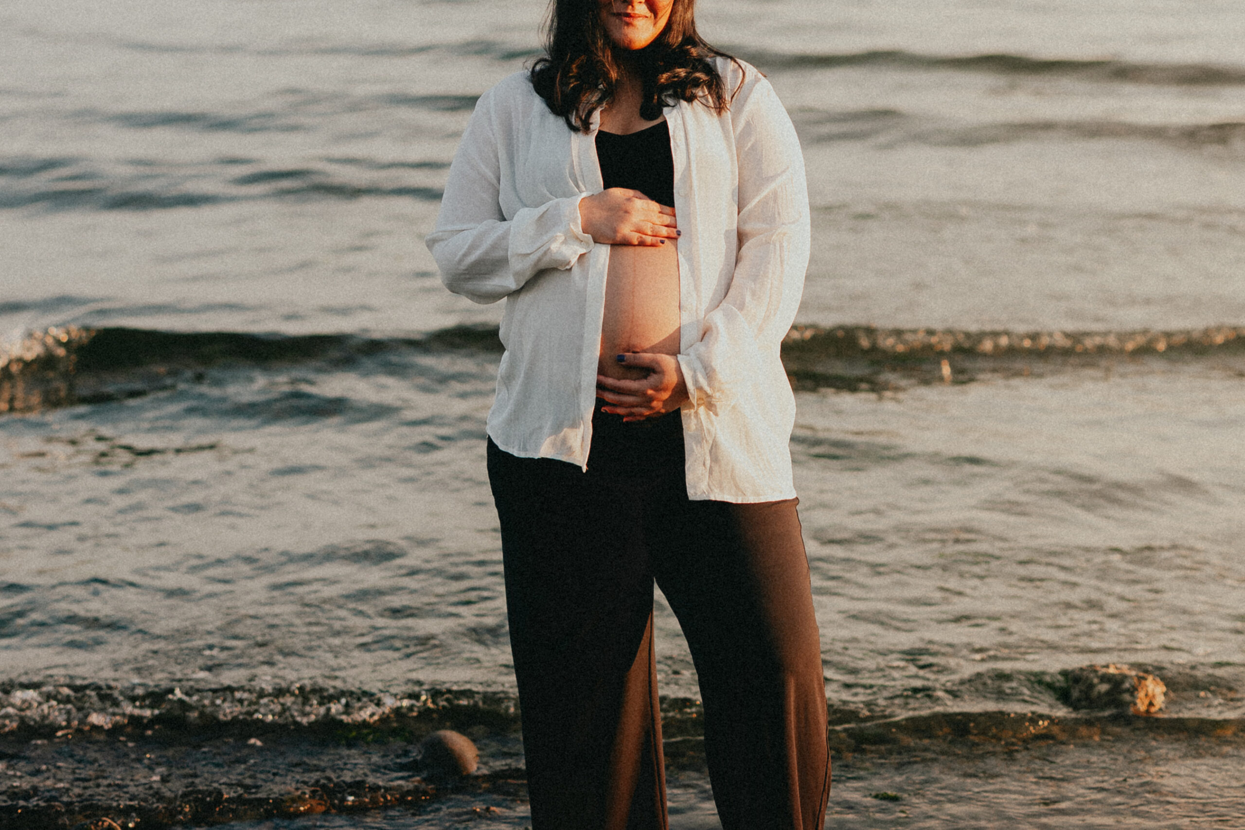 Photo of a pregnant woman standing in the ocean cradling her baby bump