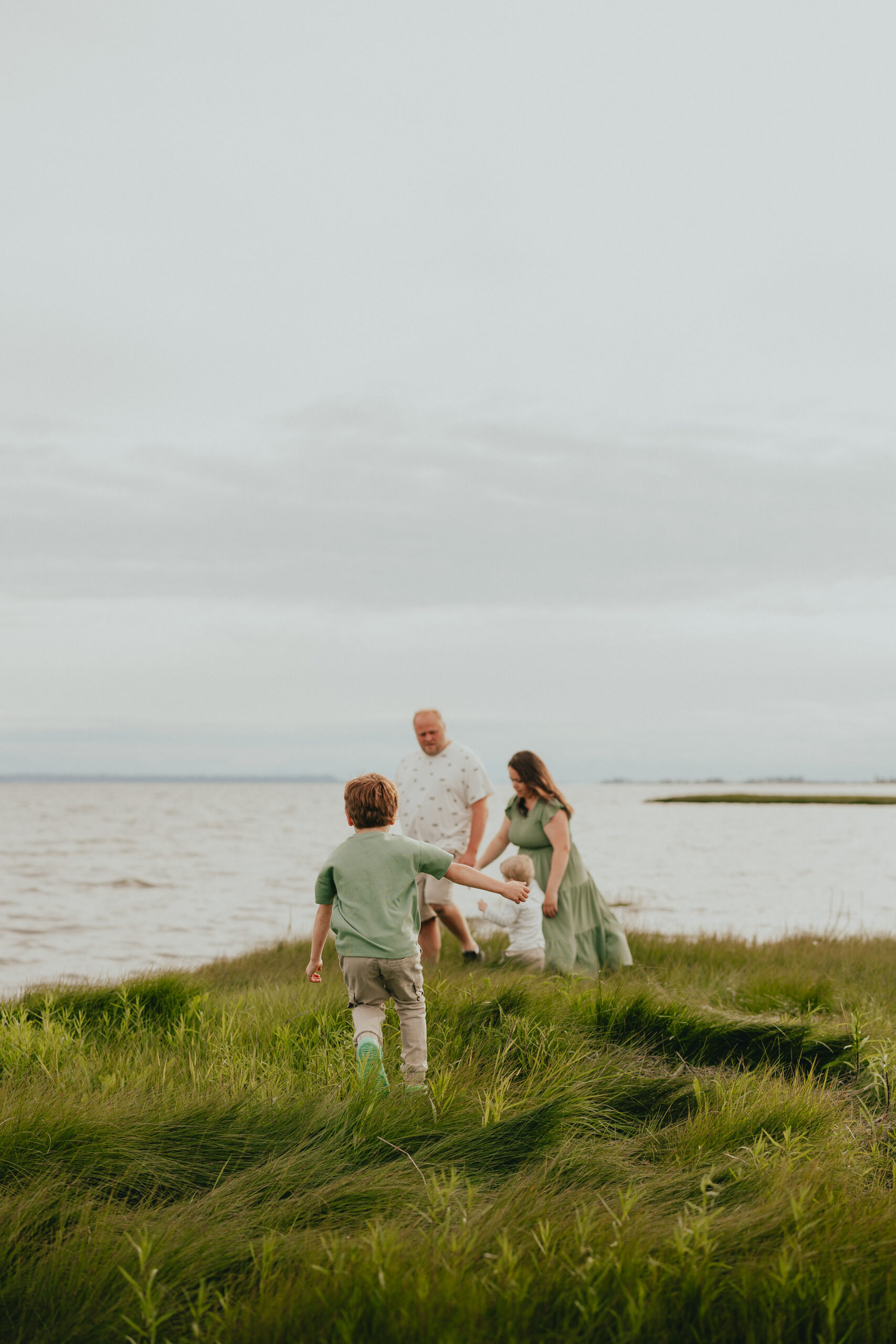 Photo of a family of 2 with 2 young boys standing by the ocean with one of the boys running towards them. Used in a blog about Langley Pools