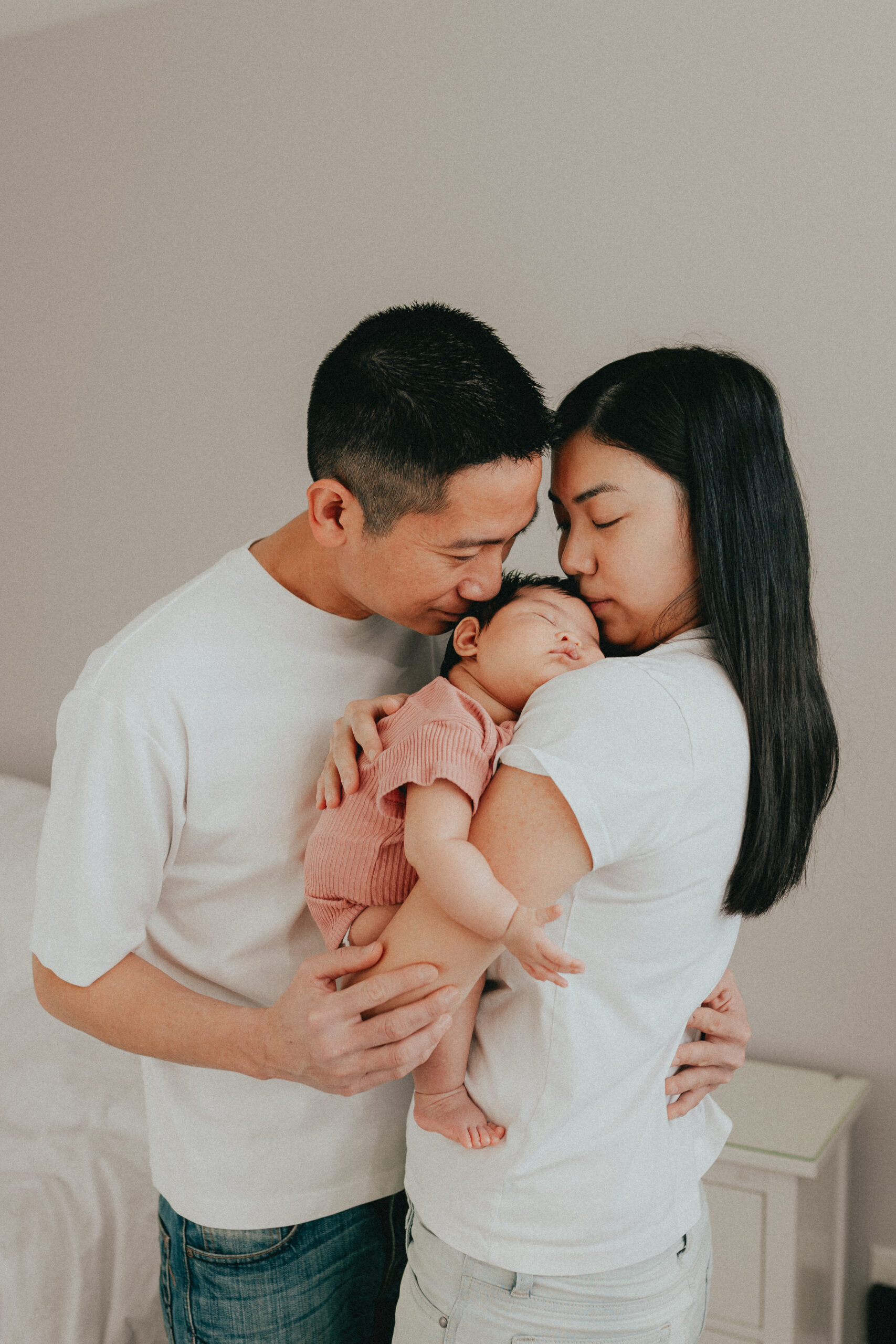 Photo of a mom holding her baby with mom and dad snuggled in close kissing her on the head. In a blog post about newborn photography tips