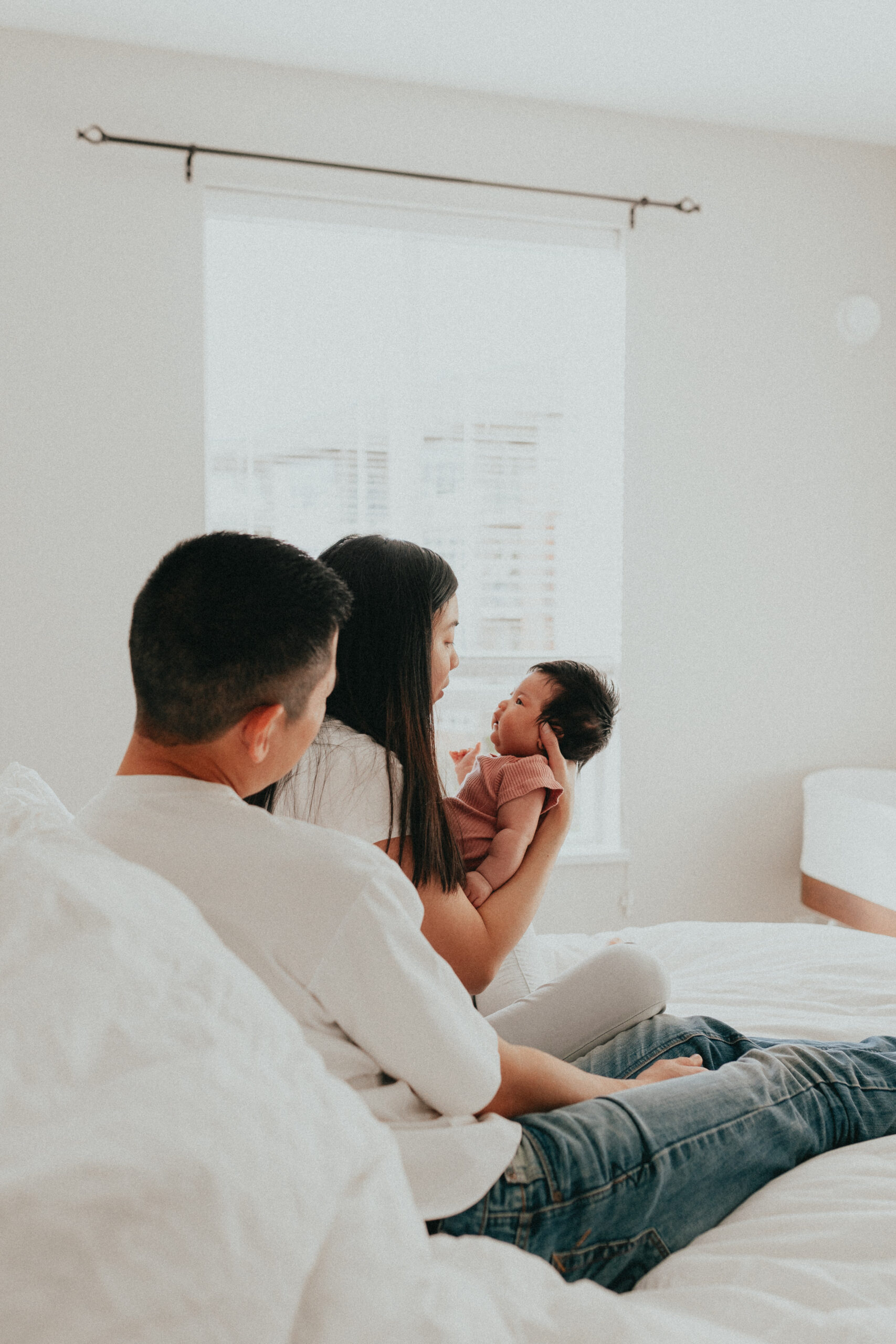 Photo of mom and dad sitting on the bed holding their baby girl. Posted for a blog about newborn photography tips