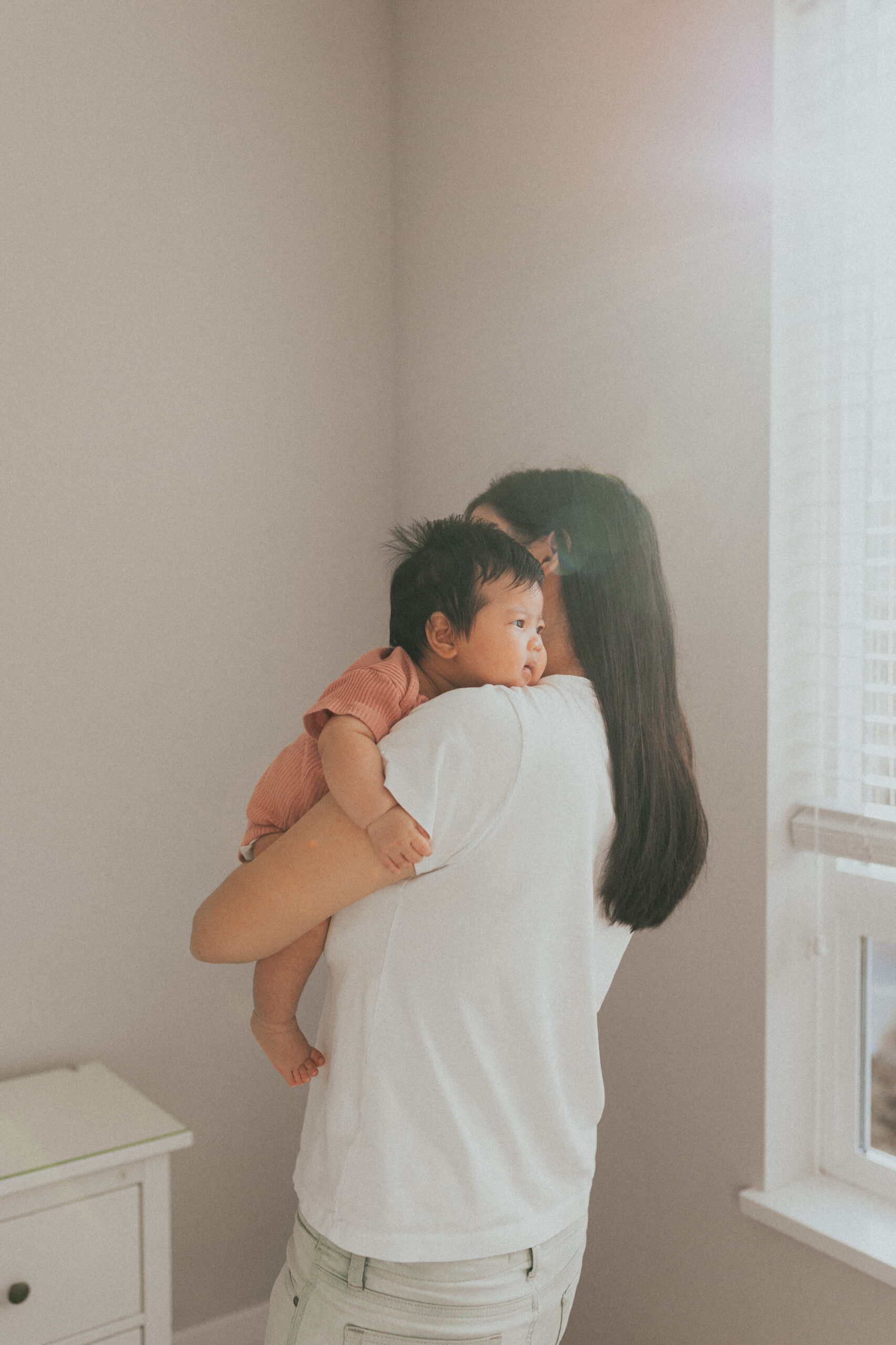 Photo of a mom holding her newborn baby over her shoulder taken so that you can see the baby's face but not moms face. Used in a blog about newborn photography tips.