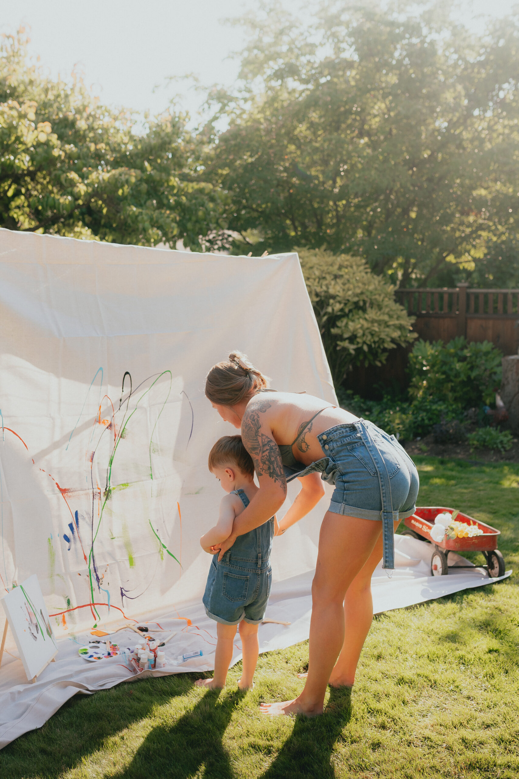 Photo of a mom and her young son standing in front of a large canvas splattering paint onto it