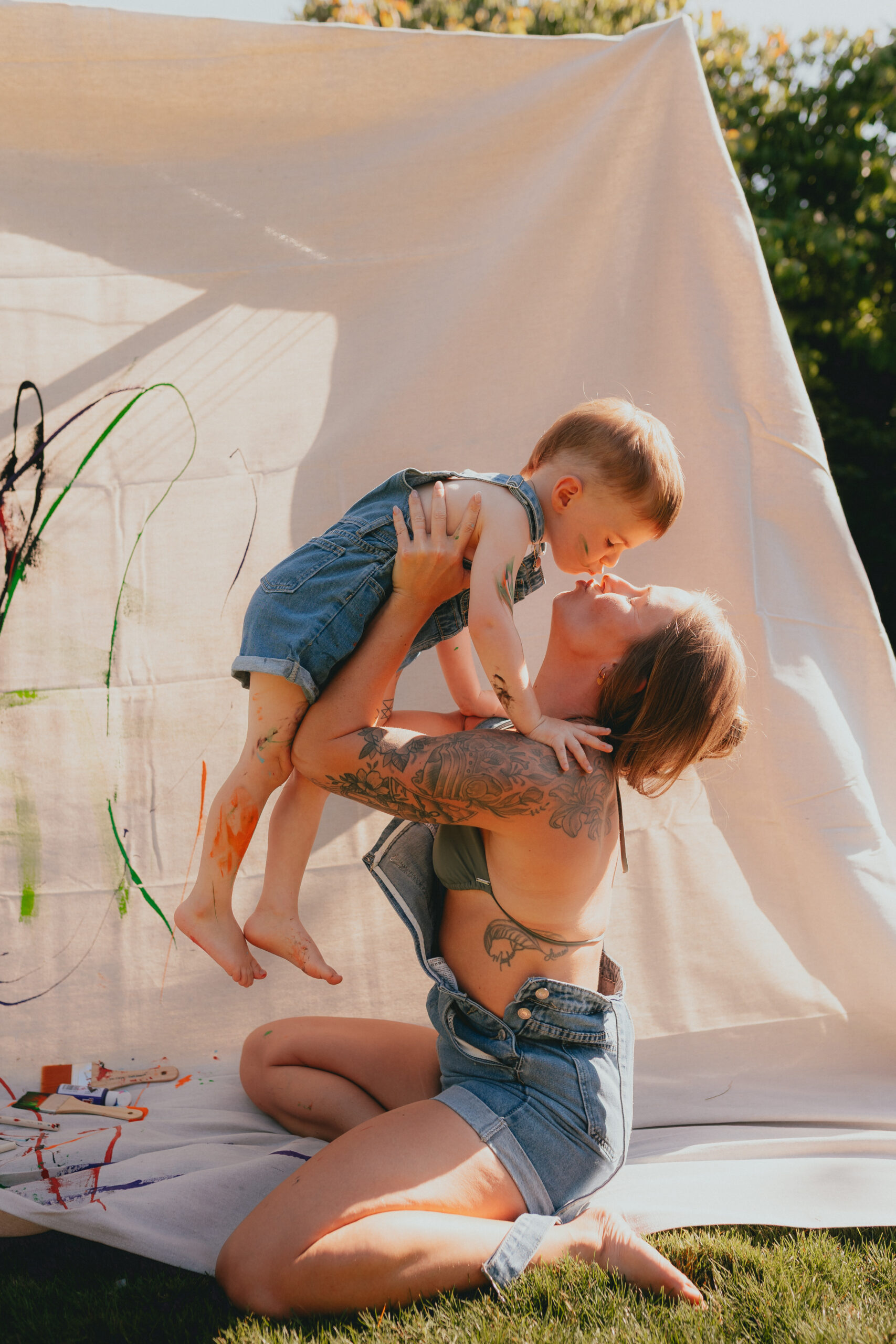 Photo of a mom holding her toddler son in the air while they kiss taken by a documentary photographer