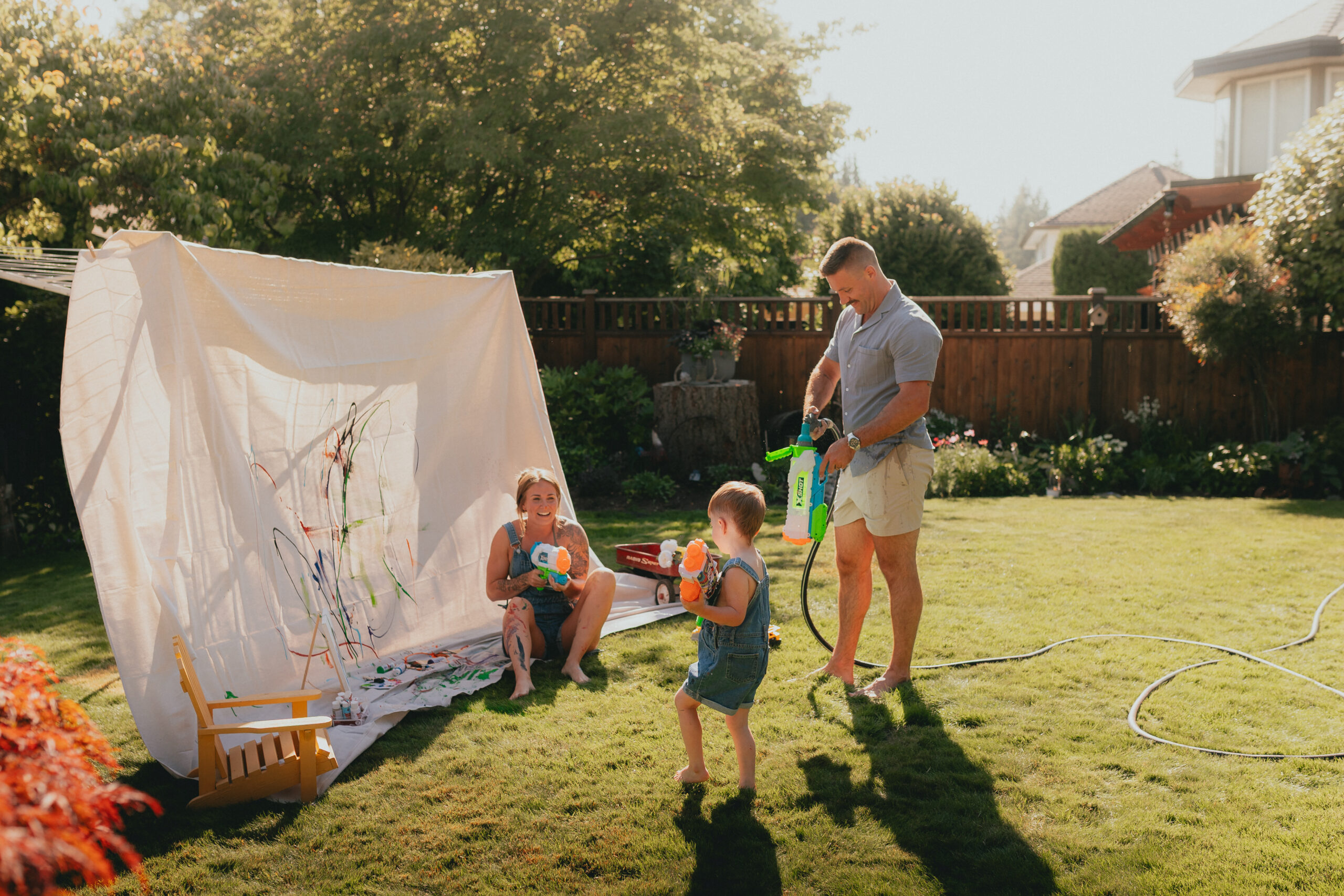 Photo of a young boy and his parents in the backyard having a water fight taken by a documentary photographer