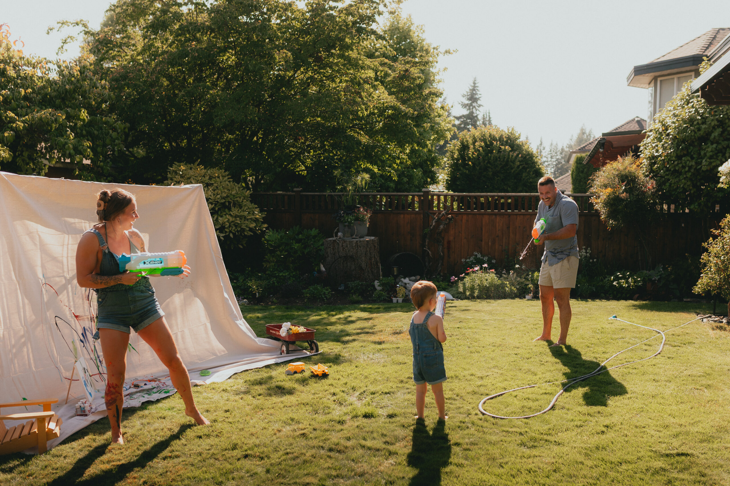 Photo of a mom and dad and their young son having a water fight in the backyard