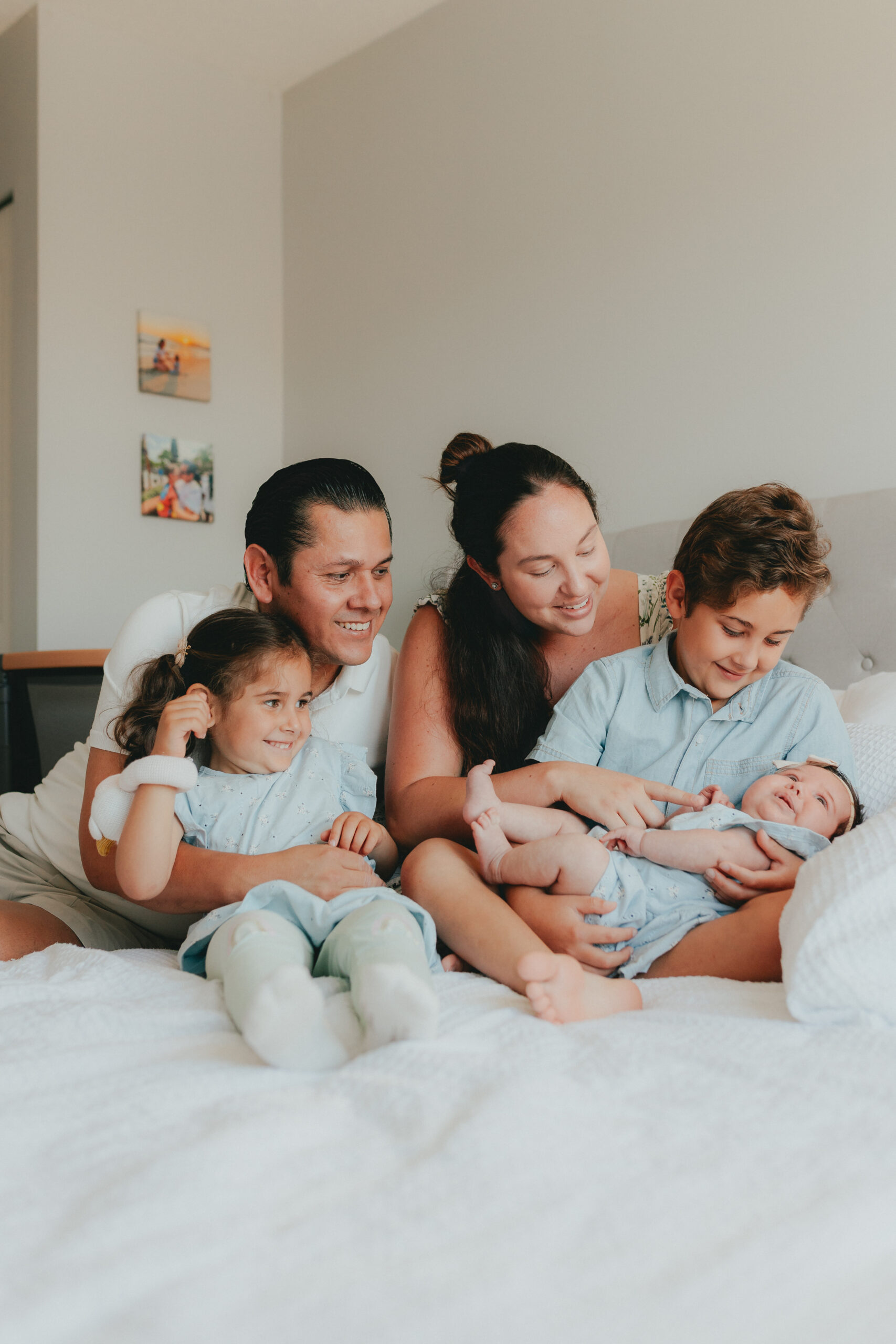 Photo of a family of 5 snuggled on the bed looking at the new baby sister.