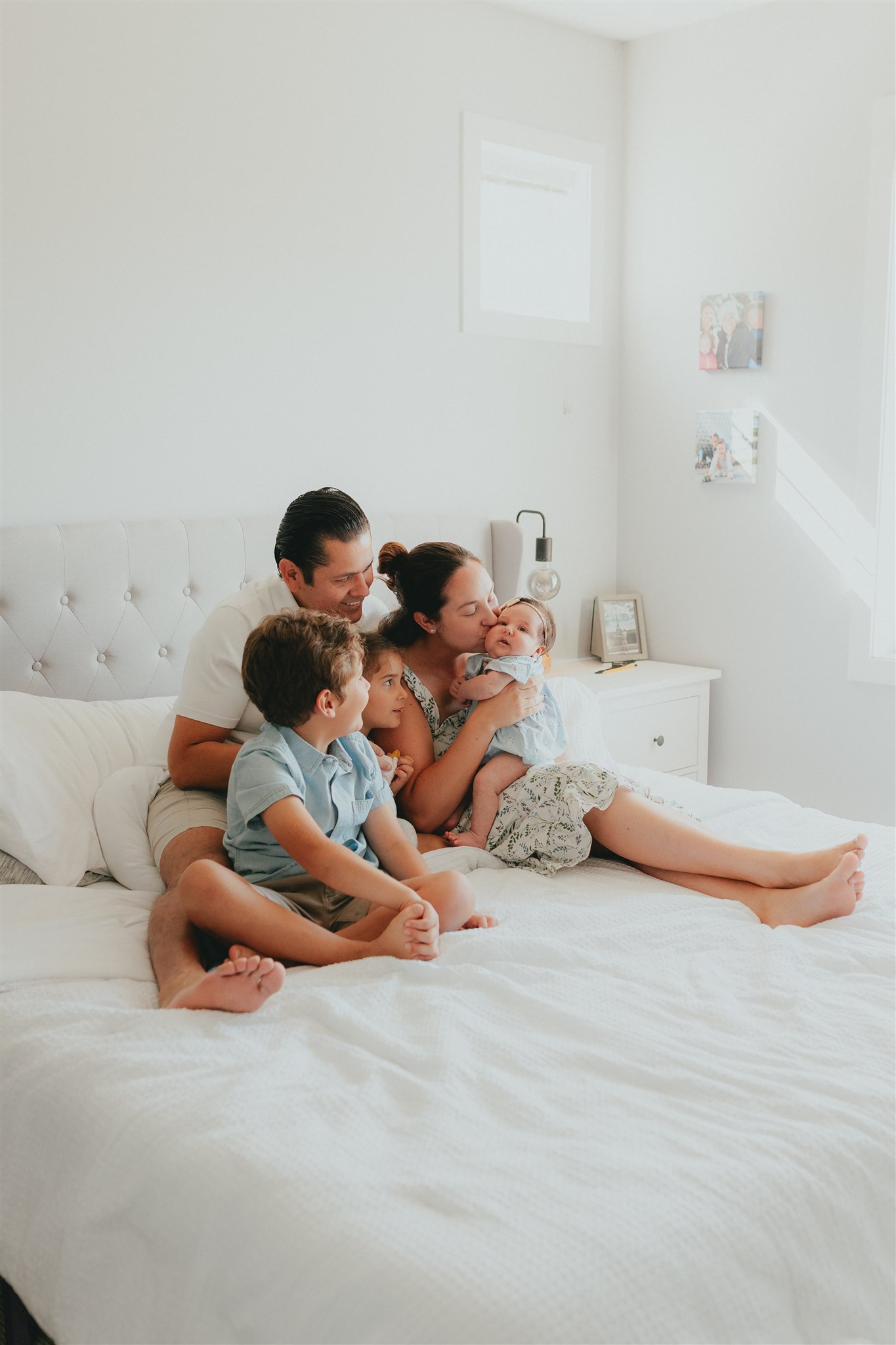 Photo of a family of 5 with a newborn baby sitting on the big bed all close together looking at their baby sister